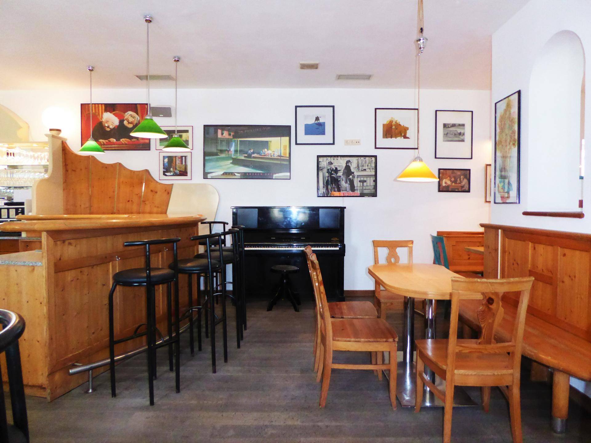 Barbereich mit Holzbänken, Tischen und einem Klavier, dekoriert mit verschiedenen Bildern an der Wand.