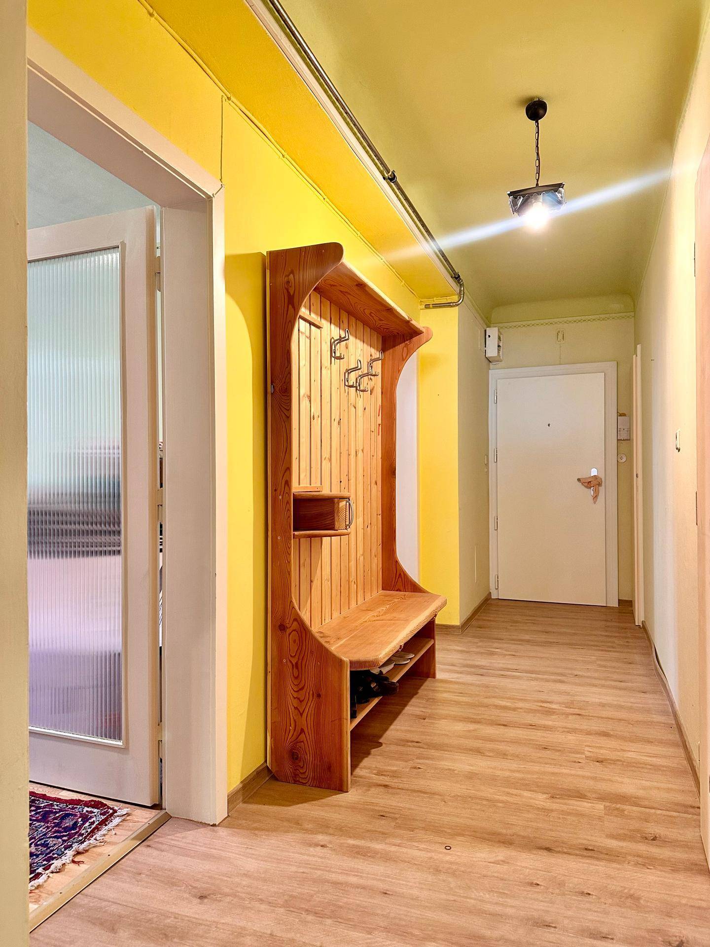 Heller Flur mit Holzparkett, gelben Wänden und einer rustikalen Garderobe.