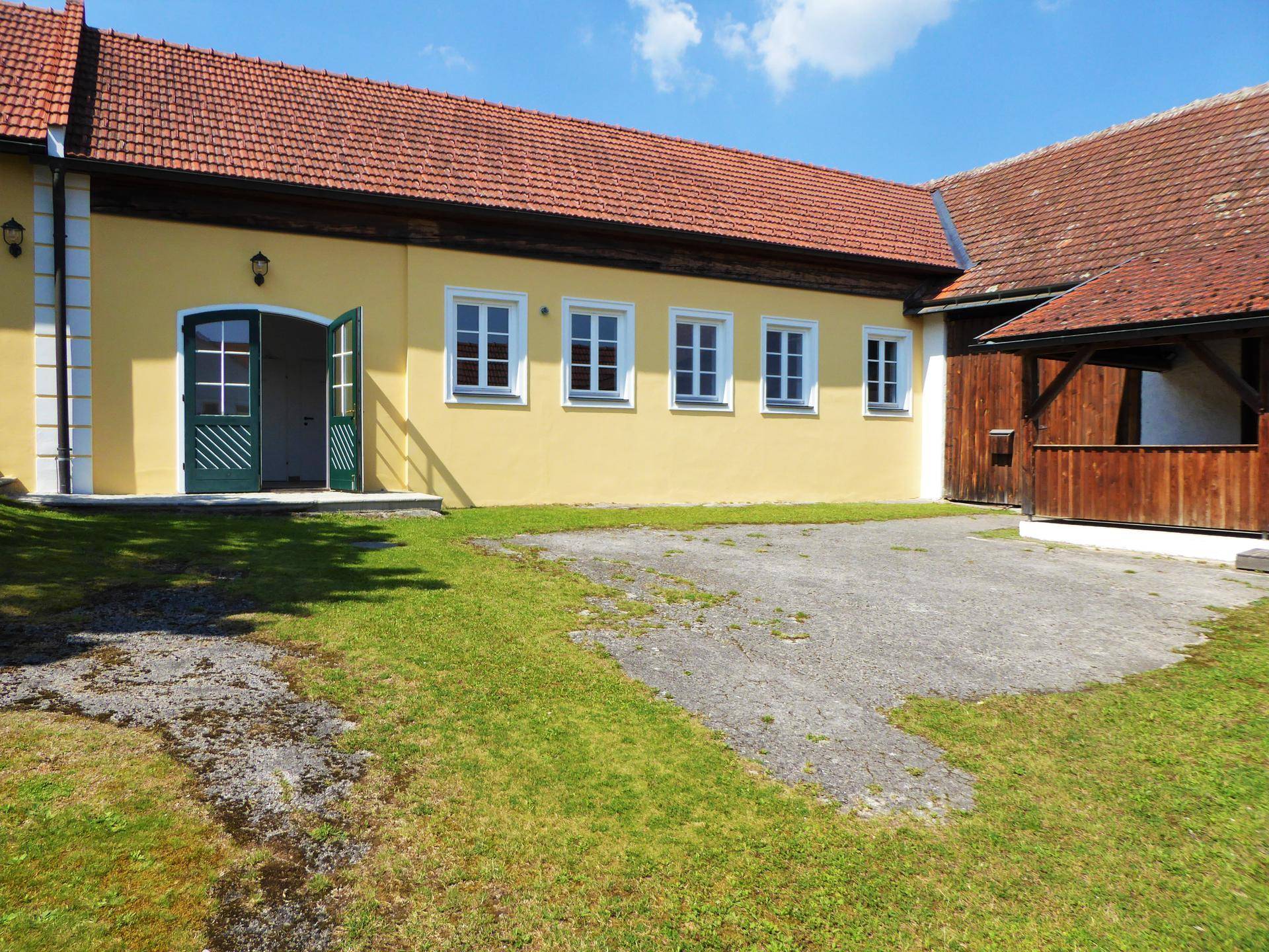 Gelbe Fassade eines traditionellen Gebäudes mit grünen Türen und Fenstern, umgeben von Rasen.