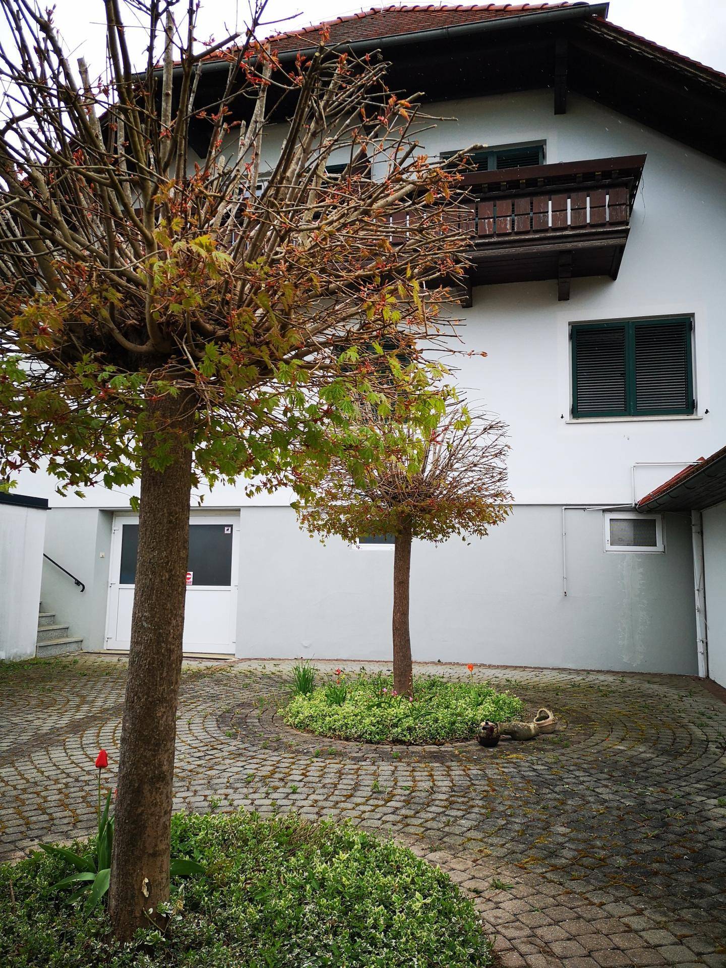 Gepflasterter Innenhof mit zwei Zierbäumen und Blumenbeeten vor einem traditionellen Haus.