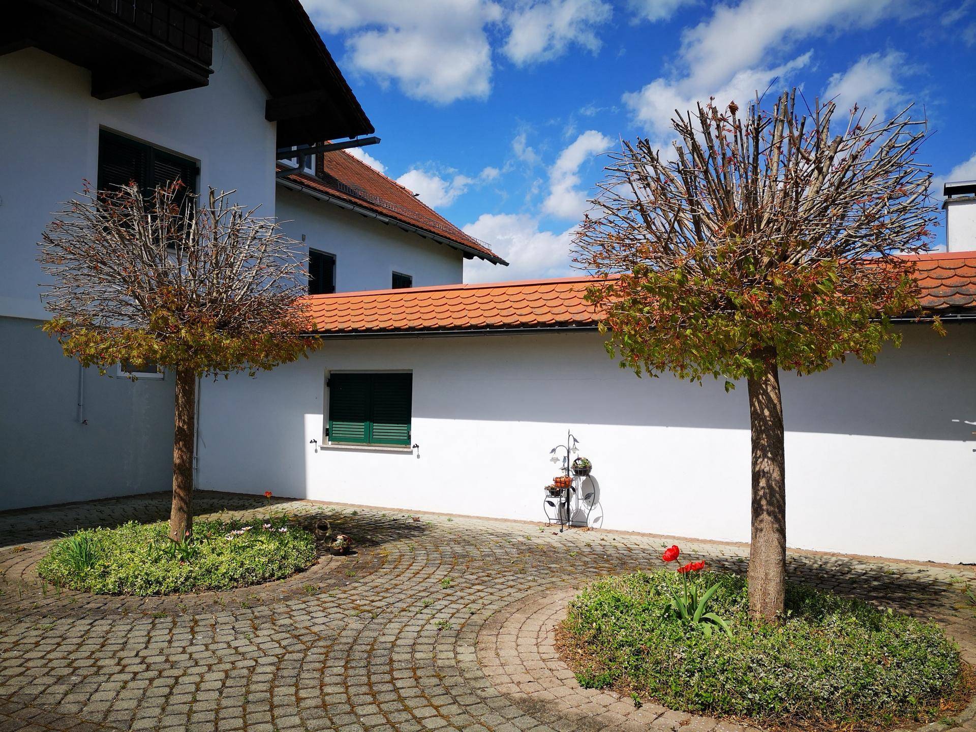 Gepflasterter Innenhof mit zwei Zierbäumen und Blumenbeeten vor einem weißen Haus.