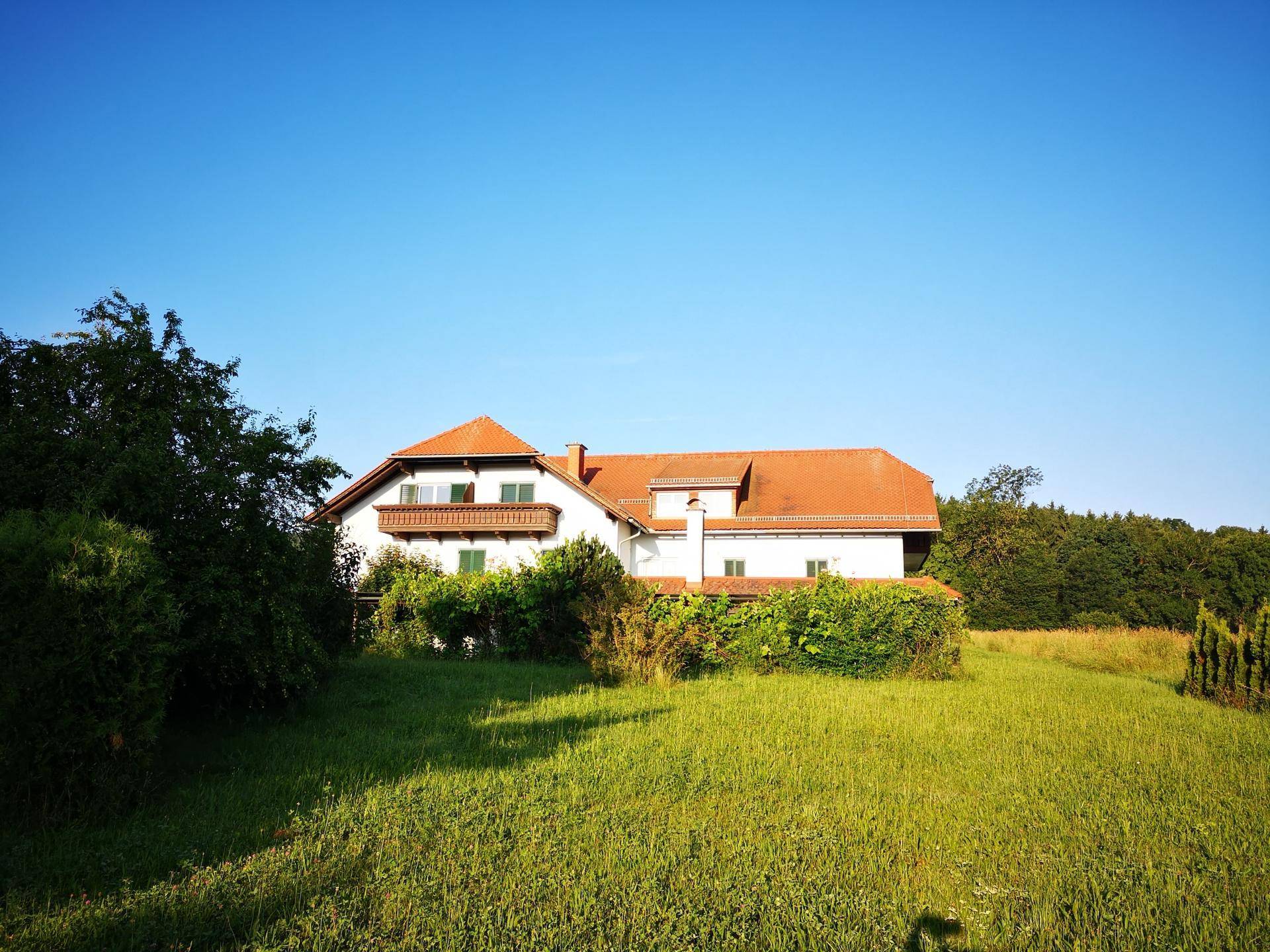 Freistehendes Haus mit rotem Ziegeldach und weitem Blick über eine grüne Wiese und Waldrand.