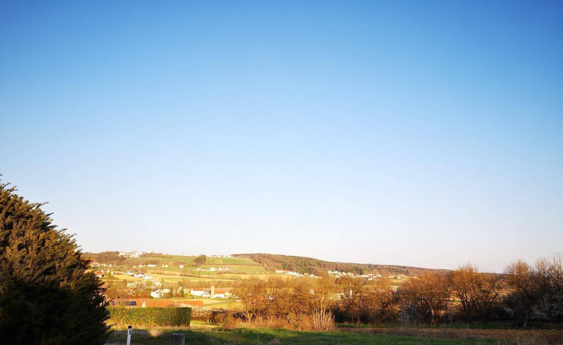 Panoramablick über eine ländliche Landschaft mit einem Dorf in der Ferne unter klarem blauem Himmel.