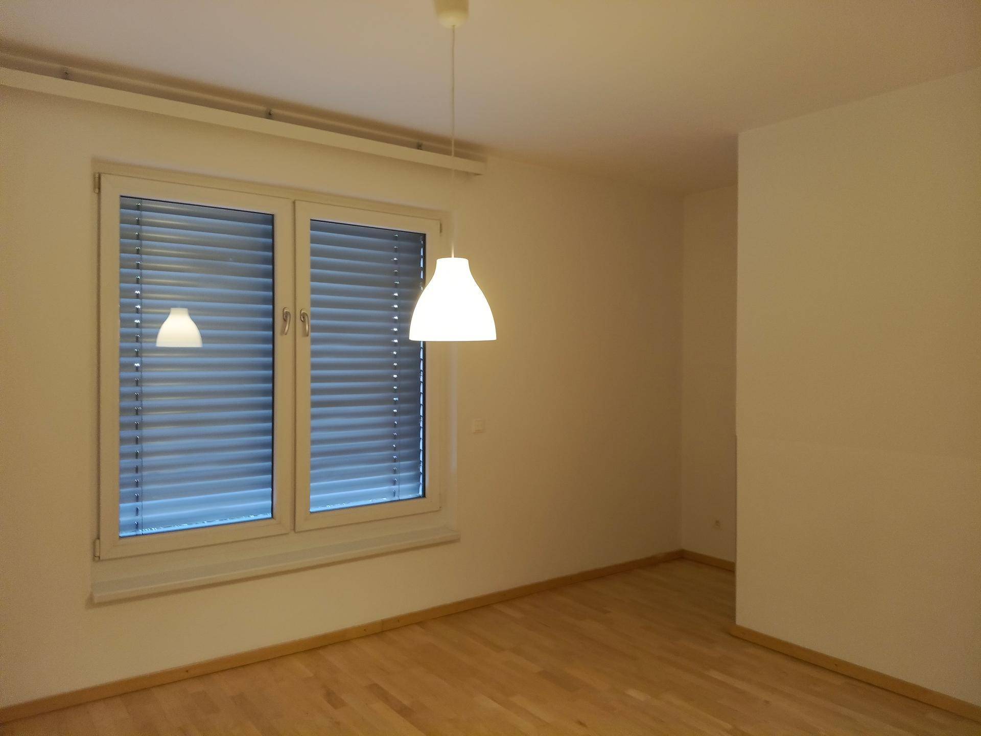 Gemütliches Schlafzimmer mit Holzboden und einem Fenster, das durch eine moderne Pendelleuchte ergänzt wird.