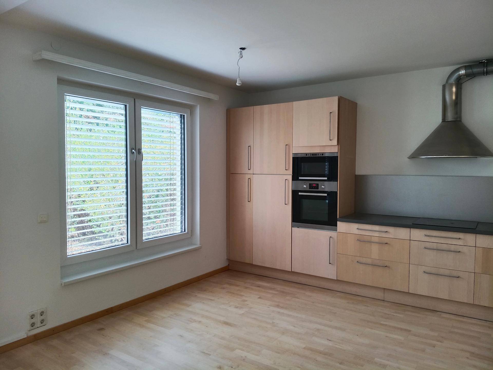 Moderne Einbauküche mit hellen Holzschränken und integrierten Geräten, neben einem großen Fenster mit Jalousien.