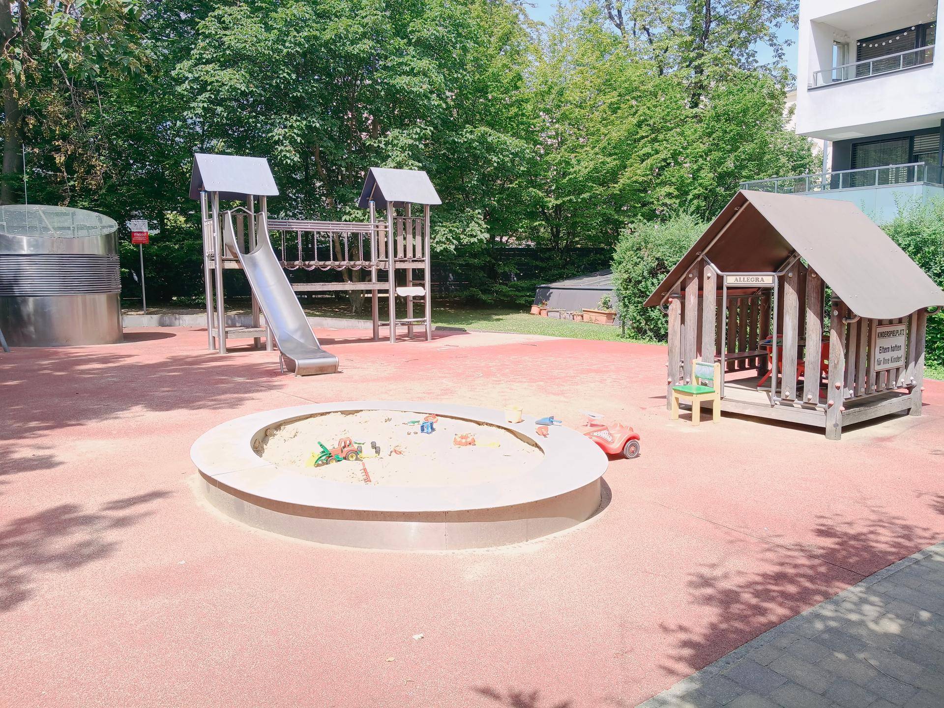 Moderner Kinderspielplatz mit Sandkasten, Rutsche und kleinem Spielhaus im Freien.
