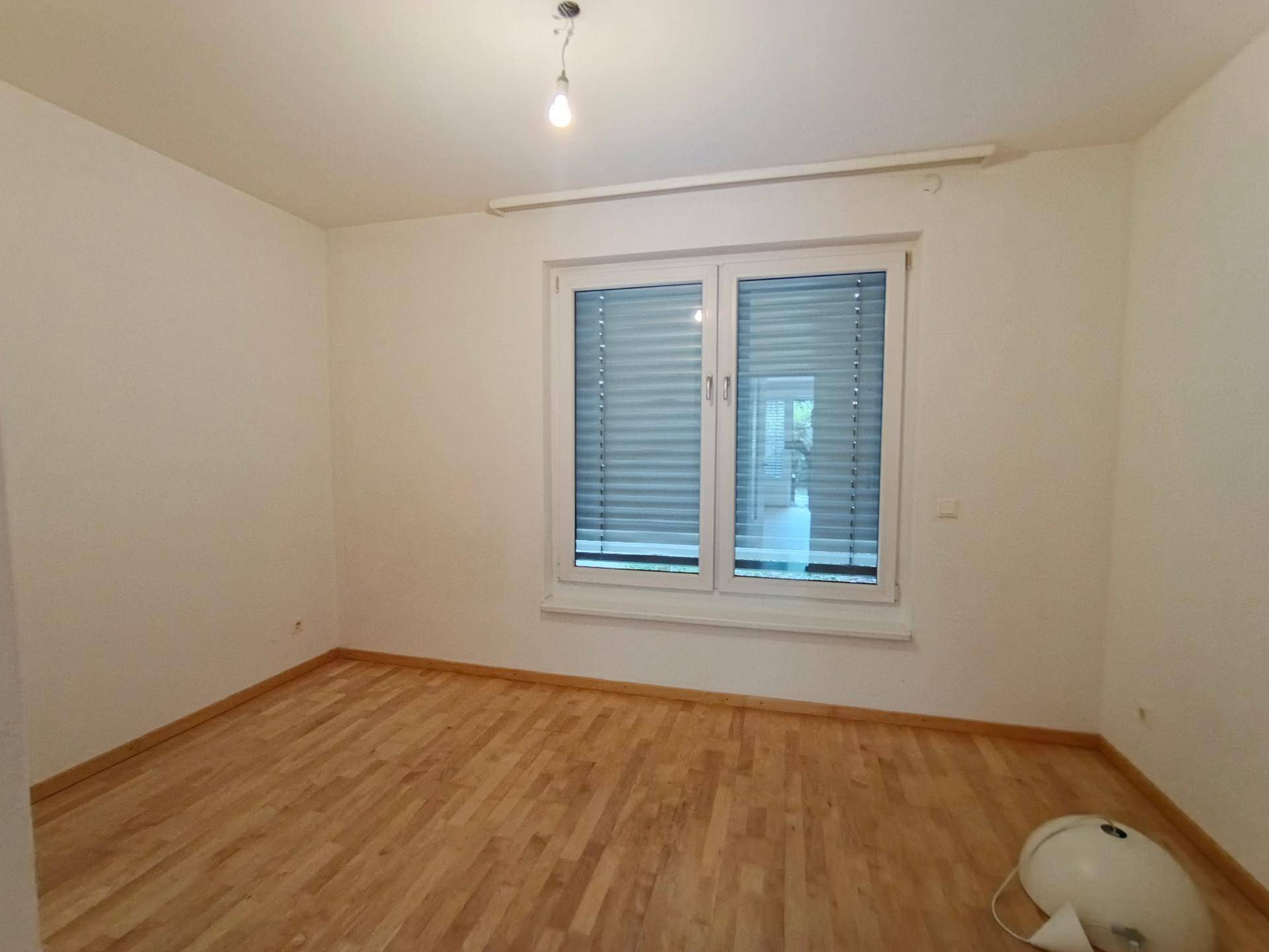 Helles Schlafzimmer mit Holzboden und einem großen Fenster, das viel Tageslicht hereinlässt.
