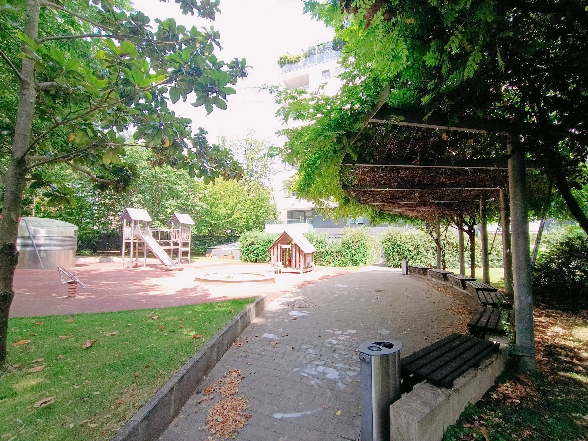 Entspannungsbereich mit Bänken unter einer Pergola neben dem Kinderspielplatz.