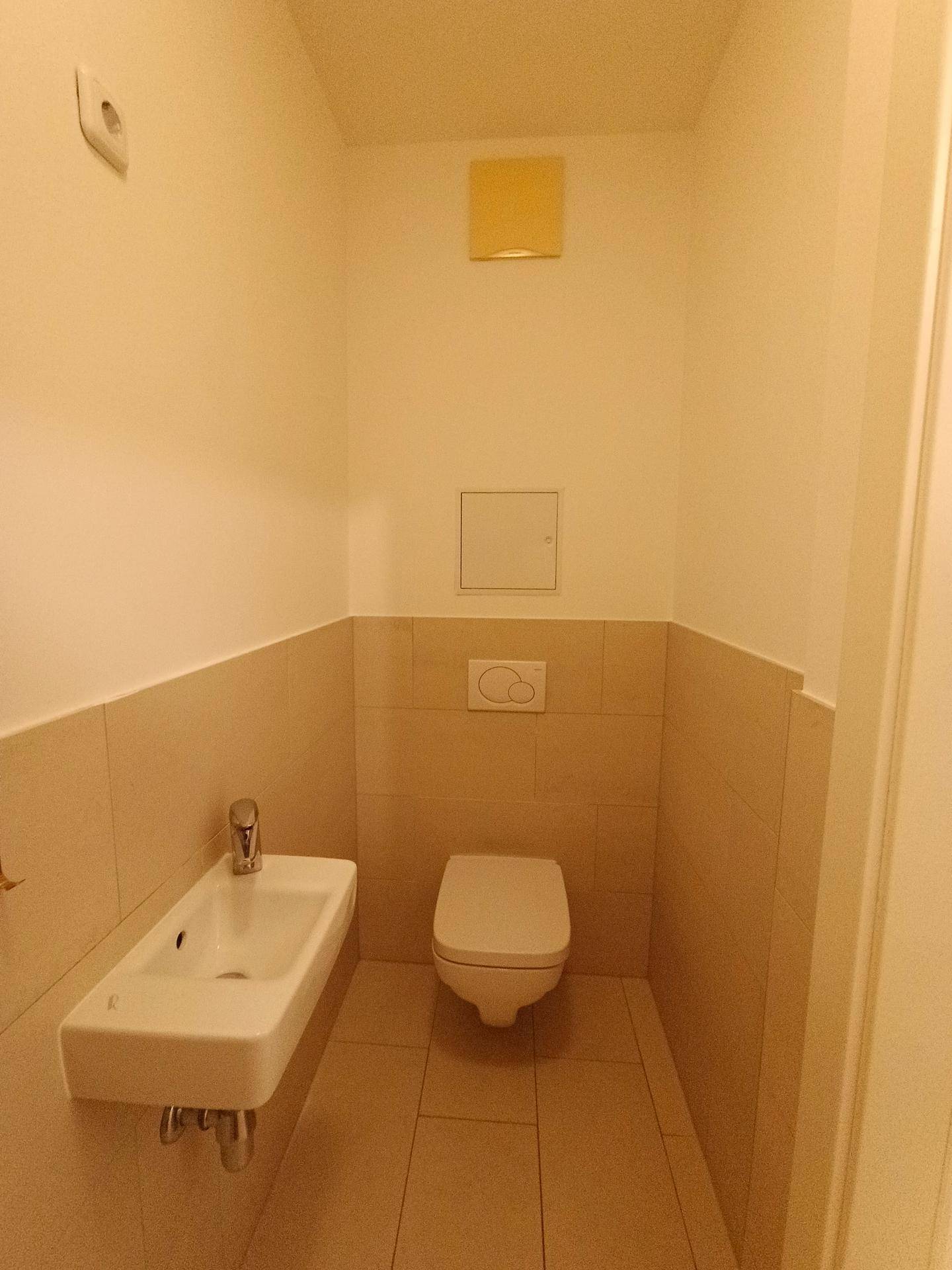 Kleines Gäste-WC mit wandhängender Toilette und Handwaschbecken, in hellen Fliesen.