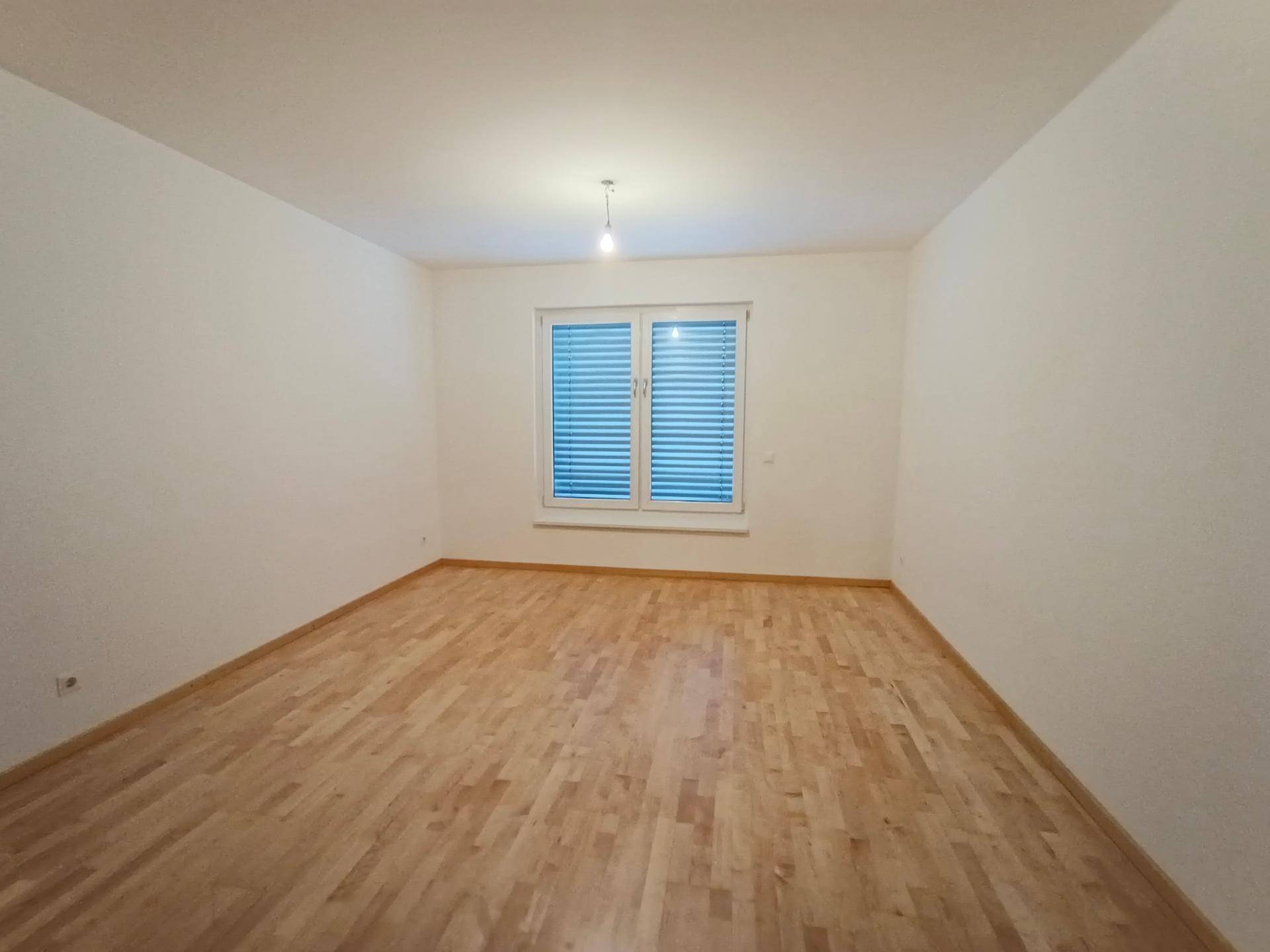 Geräumiges Schlafzimmer mit hellem Holzboden und einem Fenster, das für natürliche Belichtung sorgt.