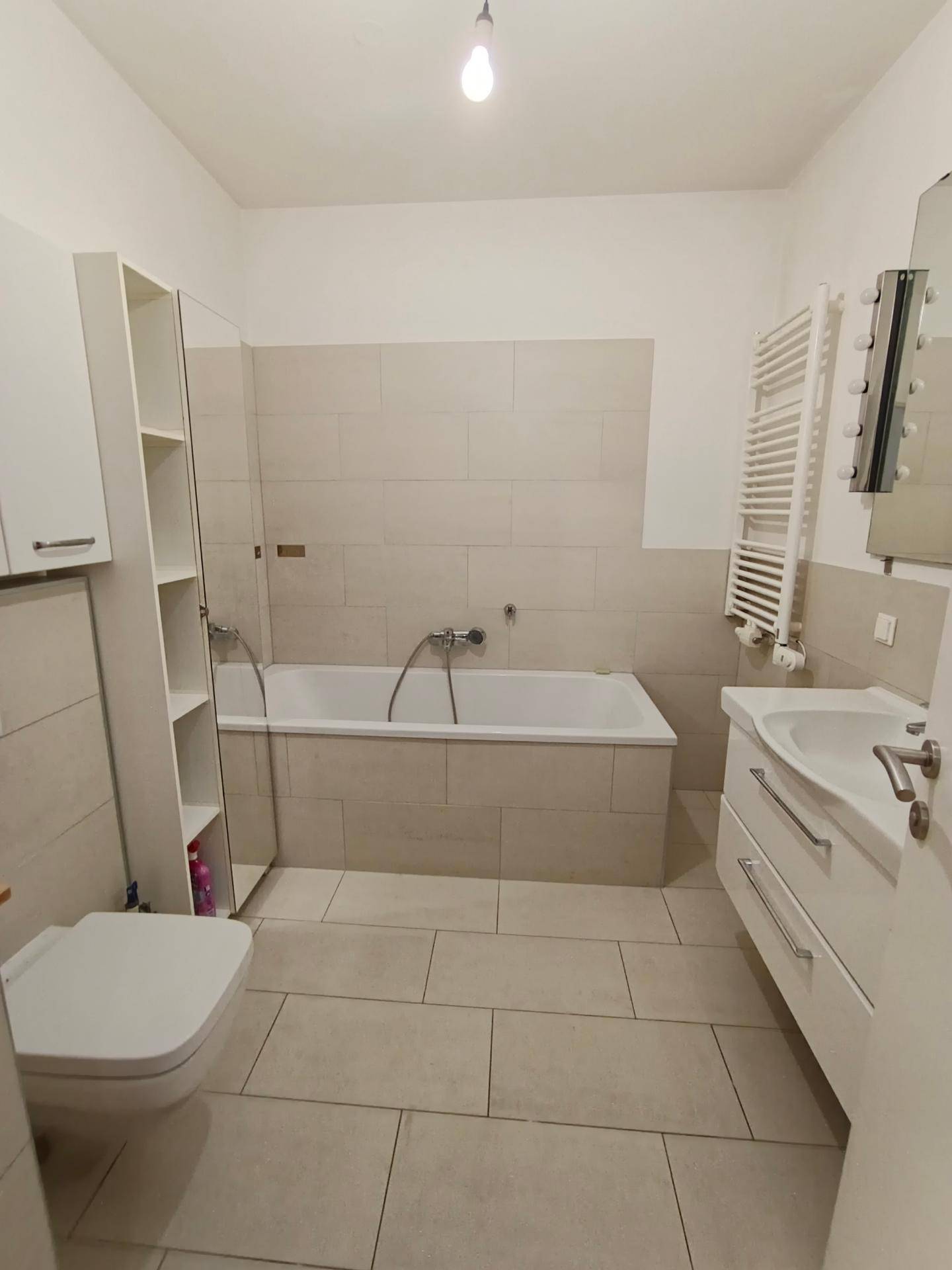 Modernes Badezimmer mit Badewanne, Waschtisch und beheiztem Handtuchhalter, in hellen Fliesen gehalten.