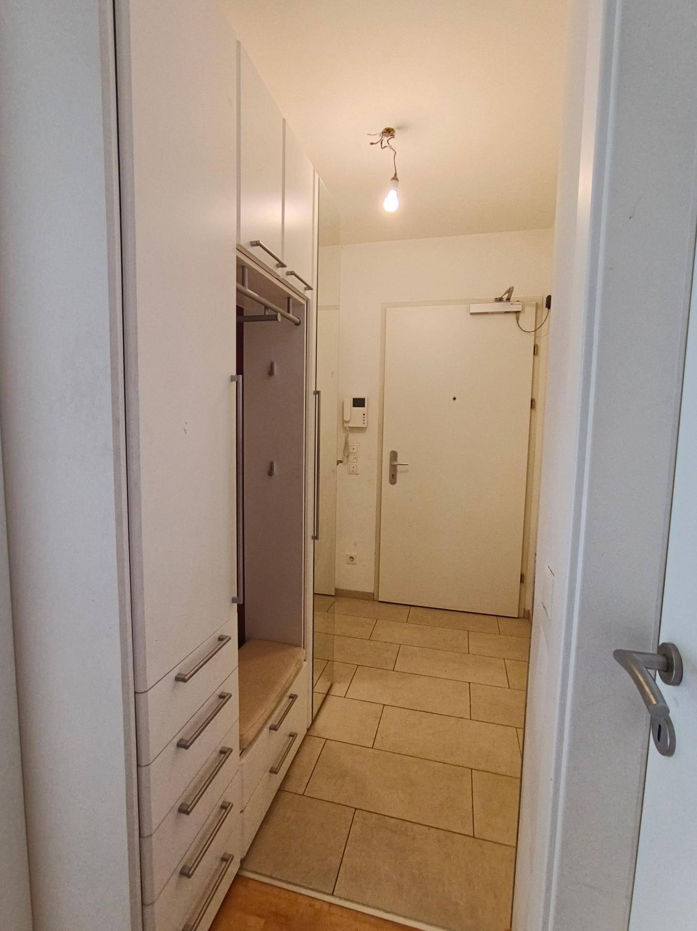 Heller Eingangsbereich mit Garderobenschrank und Fliesenboden, der zur Wohnungstür führt.