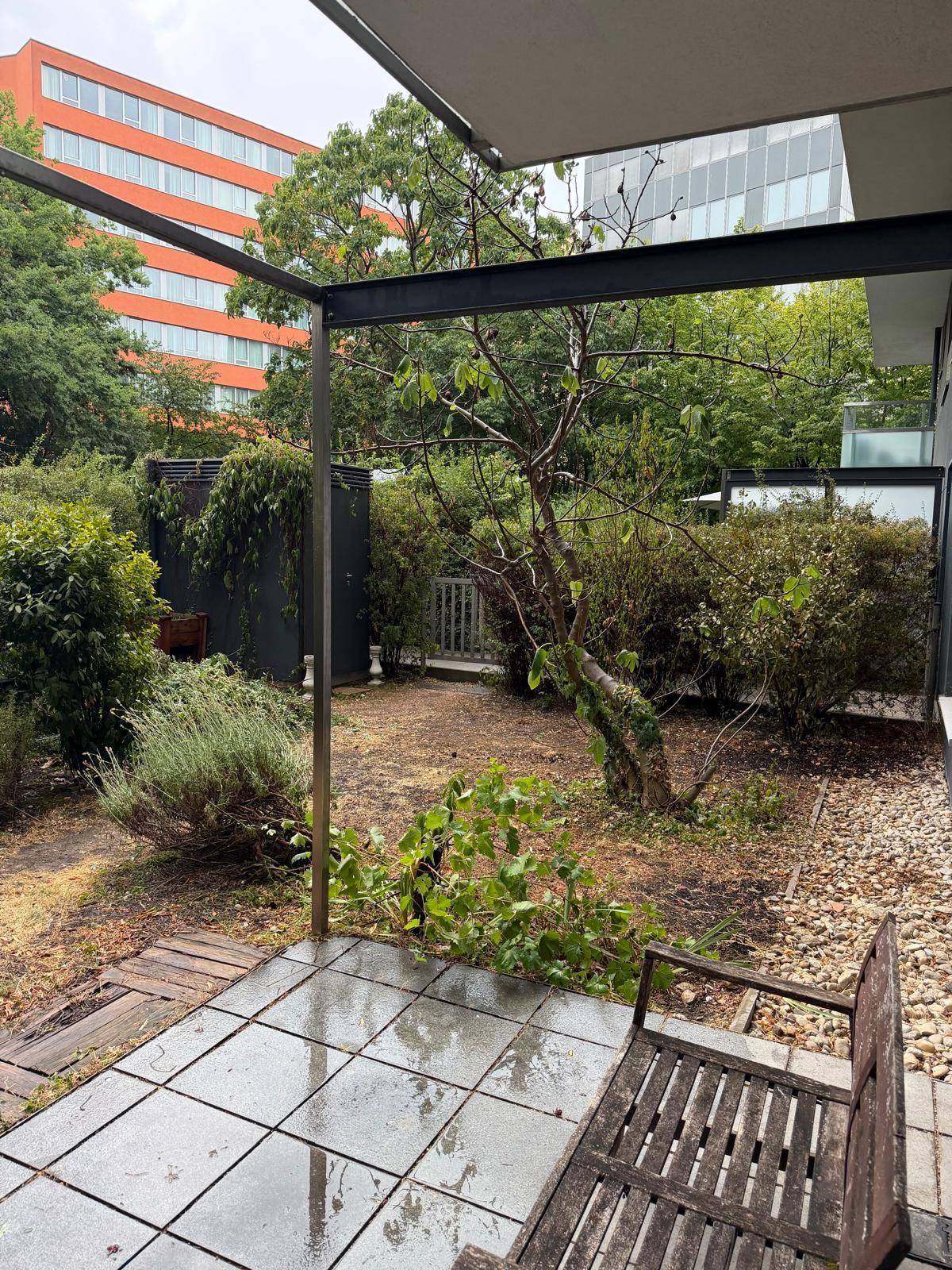 Terrasse mit Gartenbank und Blick auf den grünen Garten, umgeben von Bäumen und Sträuchern.