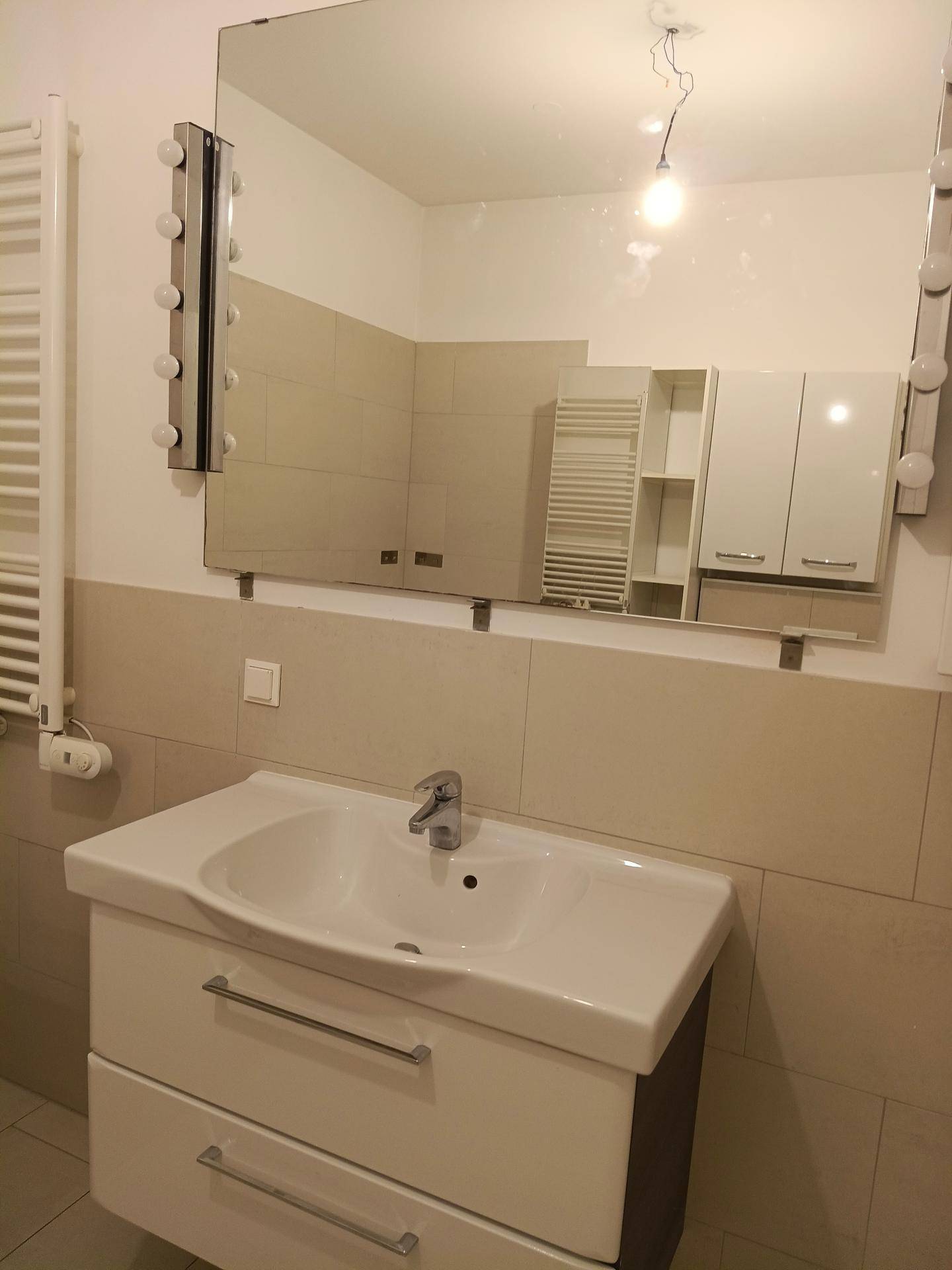 Moderner Waschtisch mit Unterschrank und großem Spiegelschrank, in einem hell gefliesten Badezimmer.