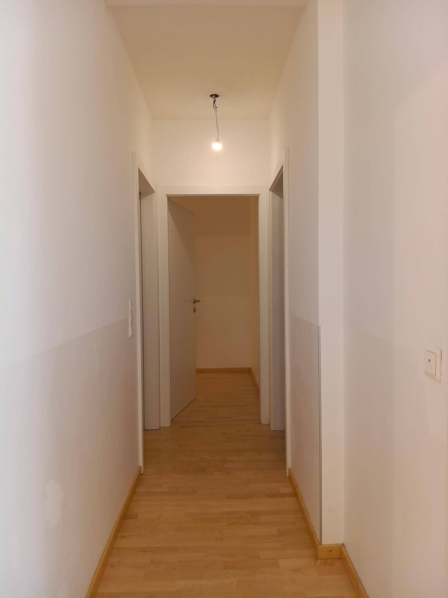 Langer, heller Flur mit Holzboden, der zu verschiedenen Räumen der Wohnung führt.