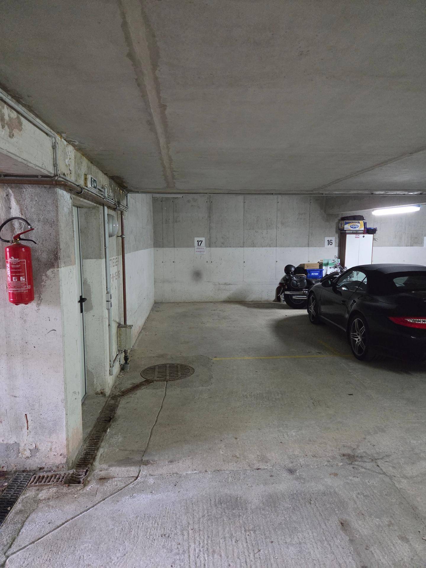 Geräumiger Tiefgaragenbereich mit Betonwänden, Feuerlöscher und Zugangstür zu den Wohnungen.