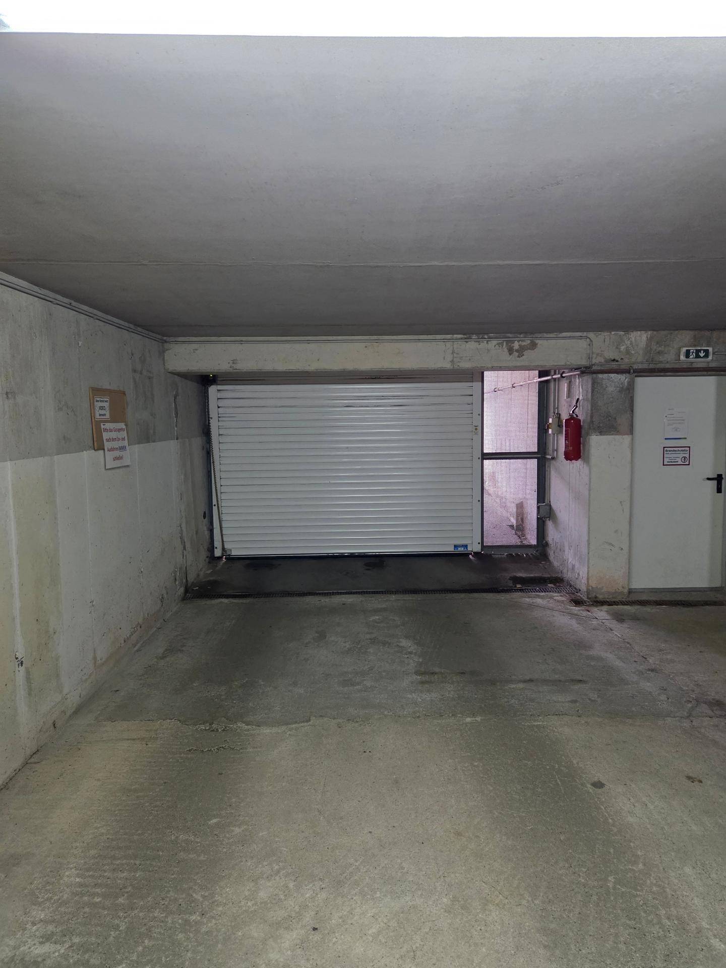 Einfahrt zur Tiefgarage mit geschlossenem Rolltor und Betonwänden, bereit zur Ausfahrt.