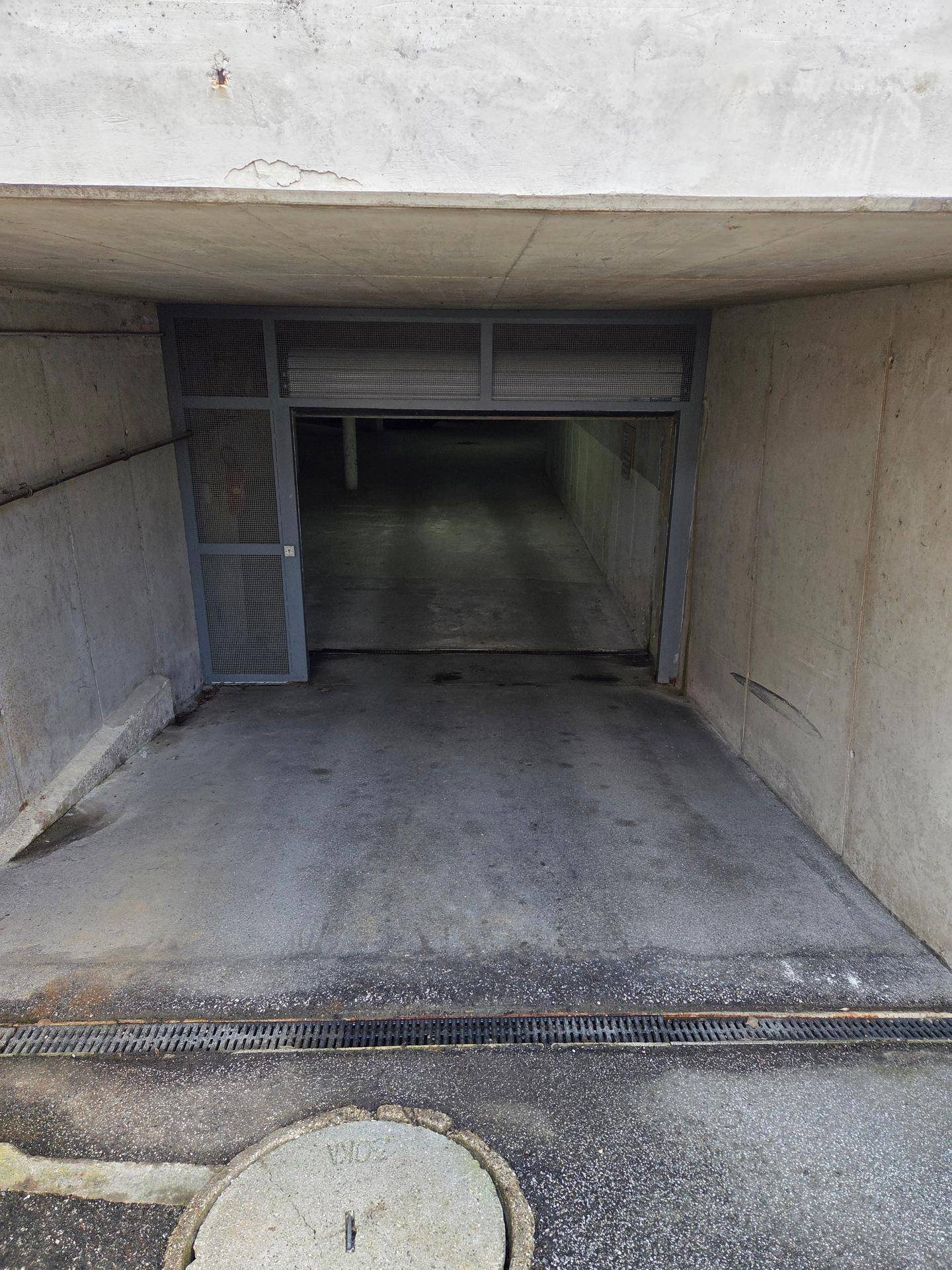 Einfahrt zur Tiefgarage mit offener Zufahrt und Betonwänden, die in die Dunkelheit führt.