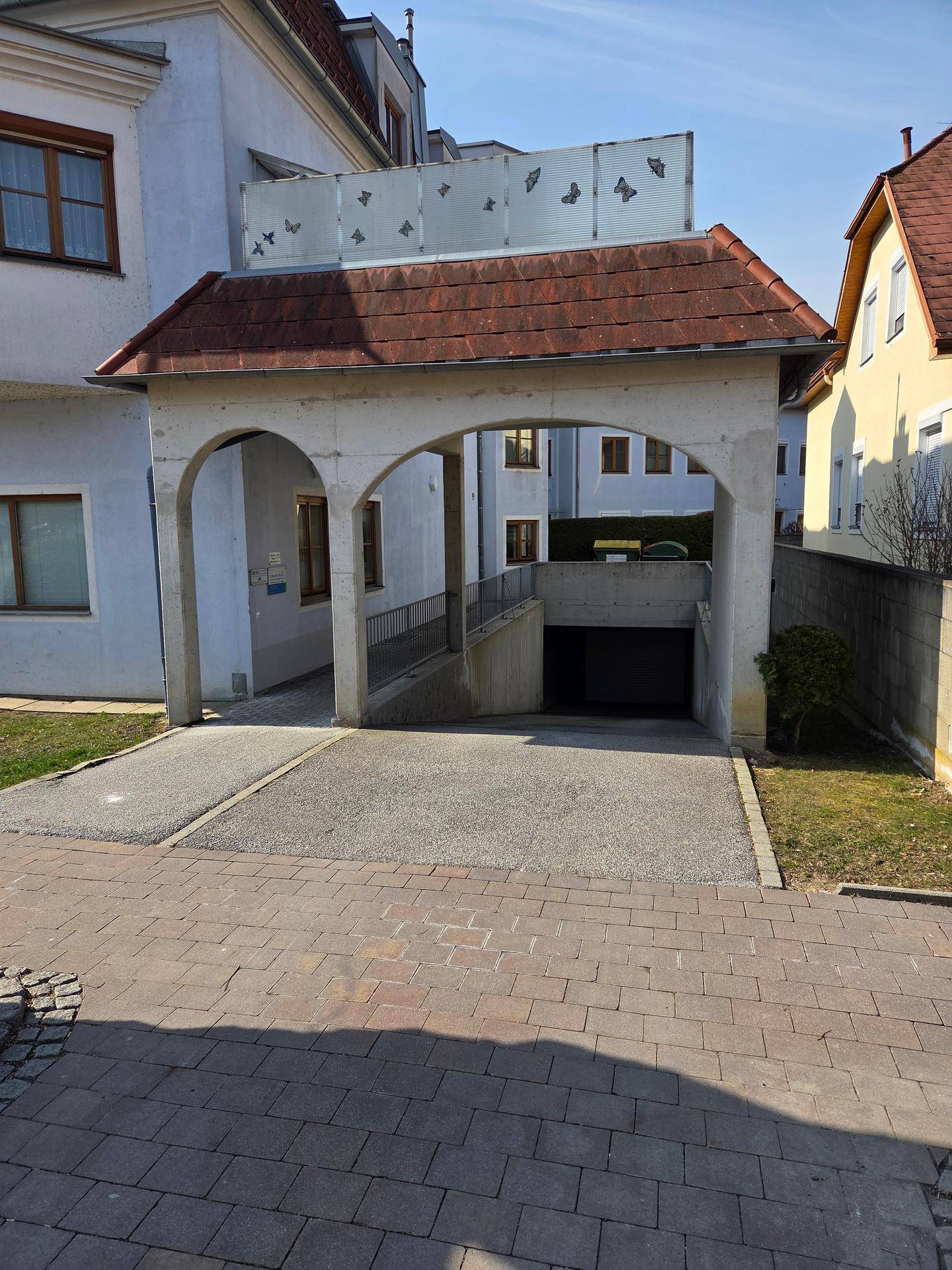 Außenansicht der Tiefgaragenzufahrt mit einem überdachten Eingangsbereich und umliegender Grünfläche.