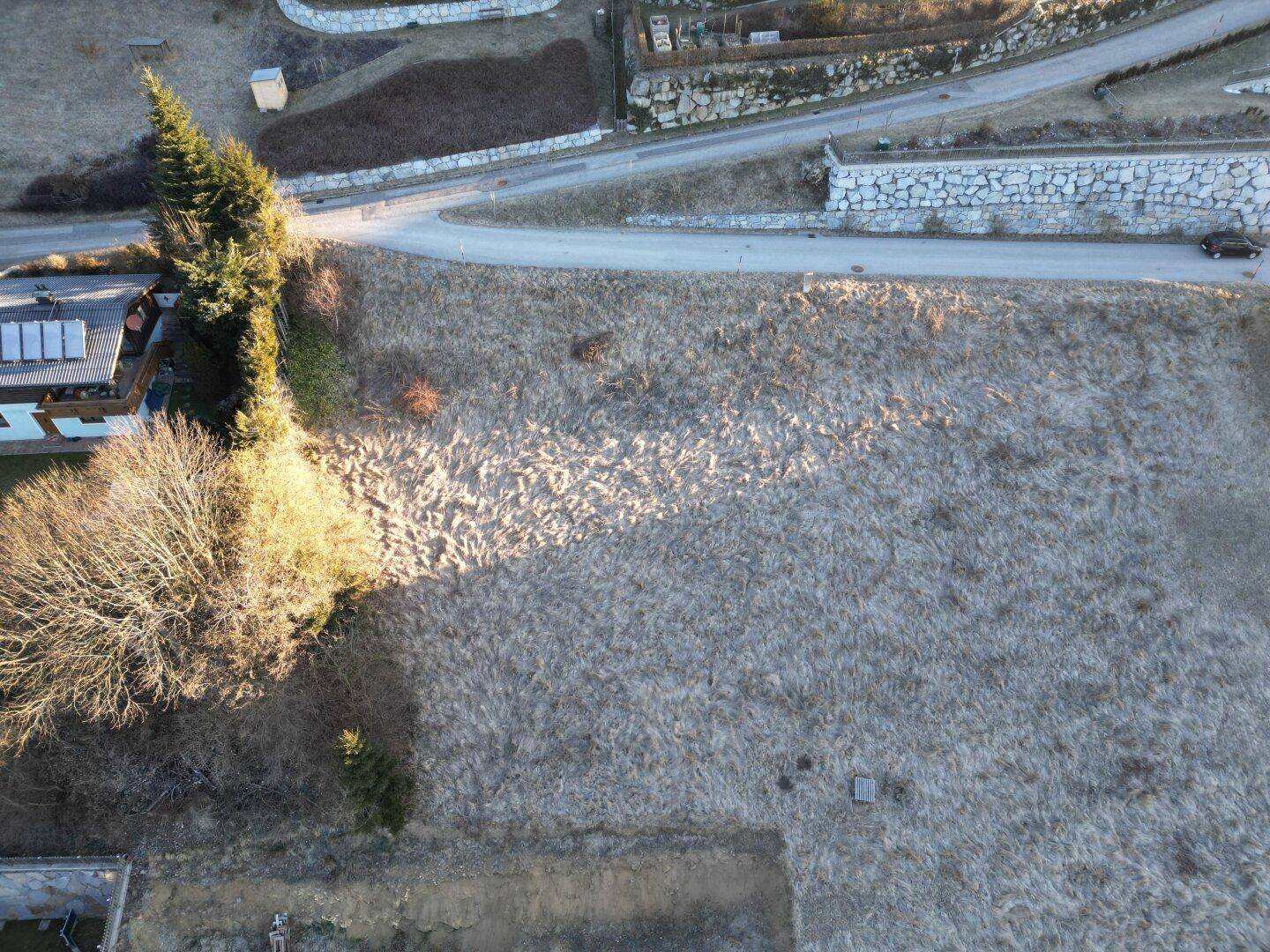 Luftaufnahme eines großen Grundstücks mit trockener Wiese, angrenzend an eine Straße und weitere Gebäude.