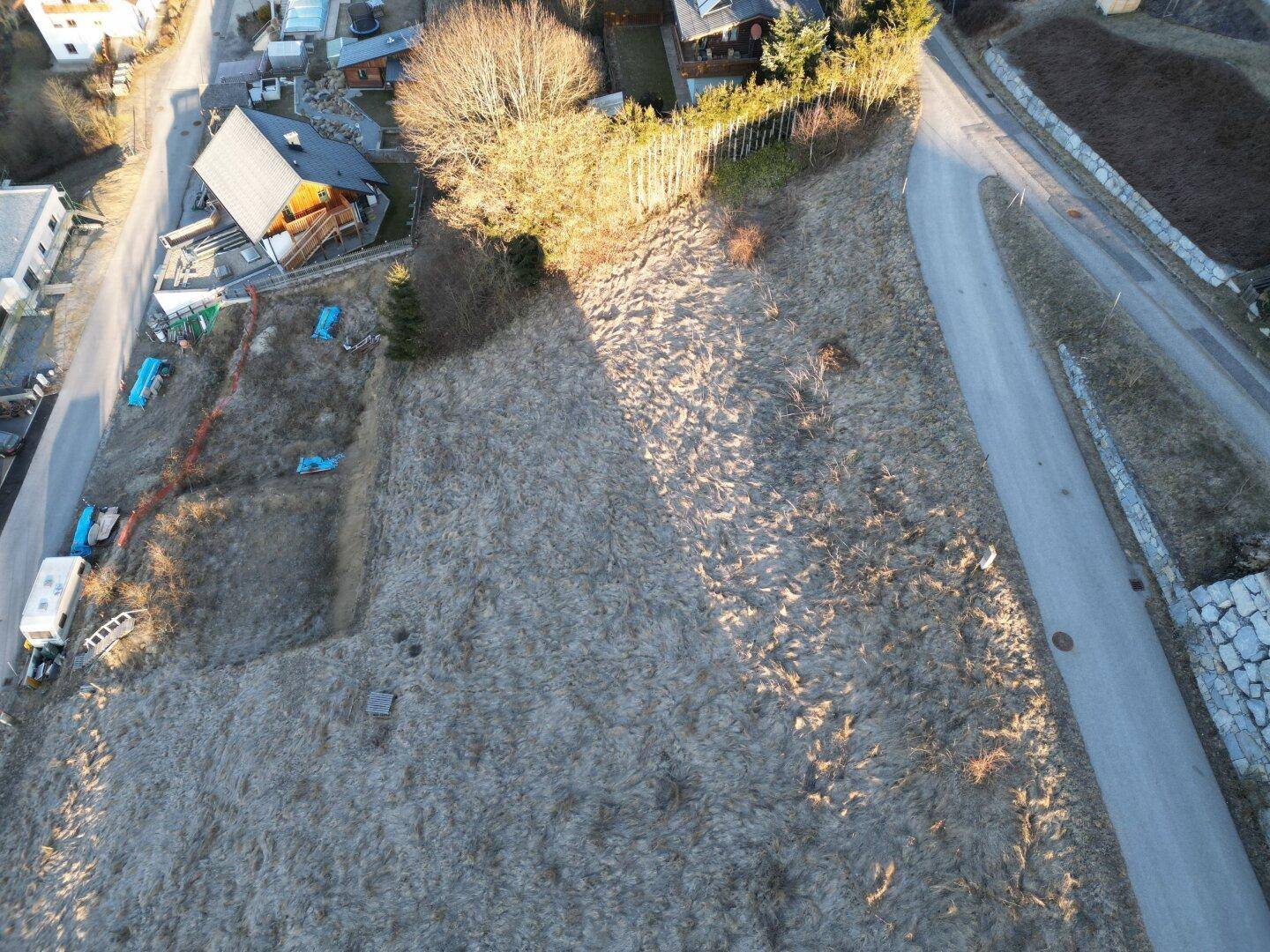 Luftaufnahme eines Grundstücks mit trockener Vegetation, umgeben von Wohnhäusern und einer Zufahrtsstraße.