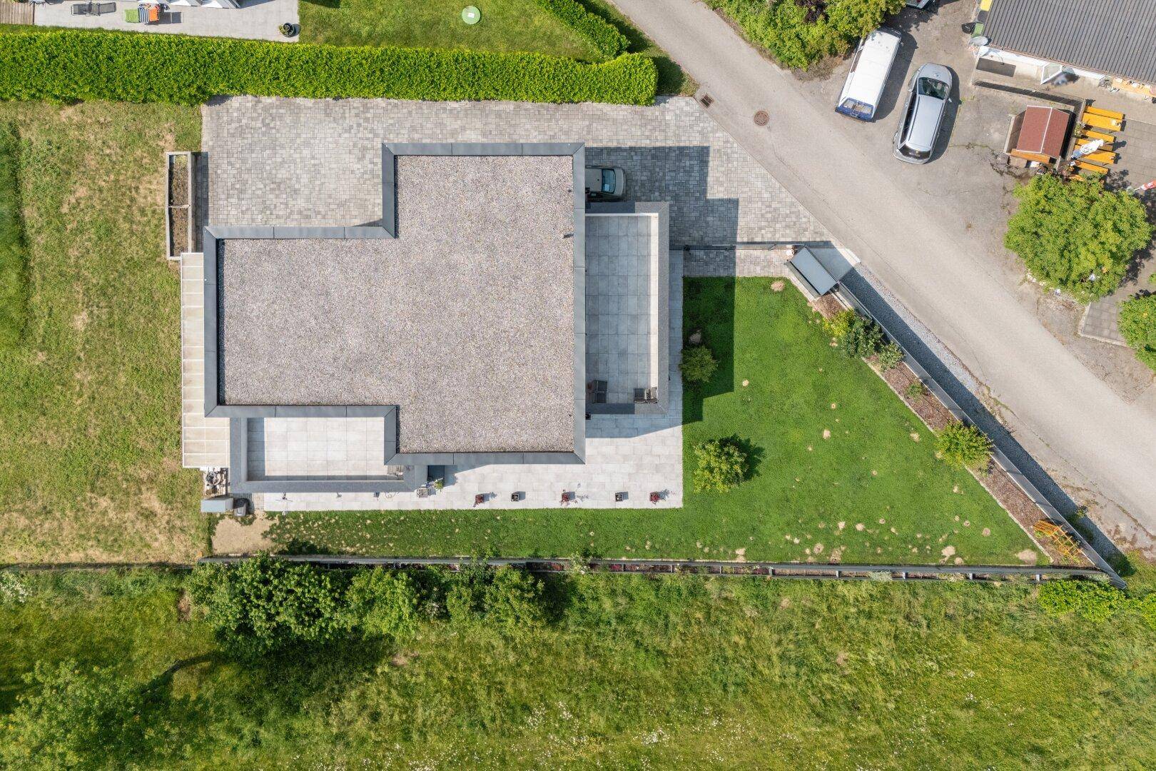 Vogelperspektive des modernen Hauses mit Flachdach, Garten und gepflasterten Außenbereichen.