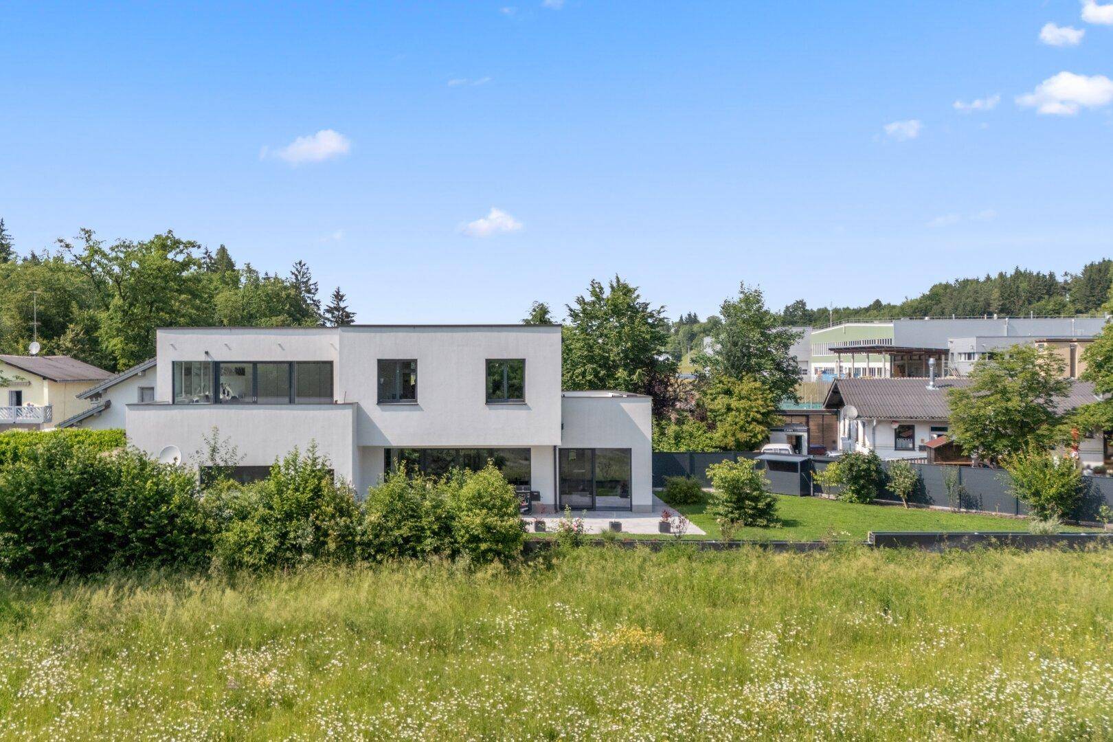 Weitläufige Ansicht des modernen Hauses in ländlicher Umgebung mit viel Grün und klarem Himmel.