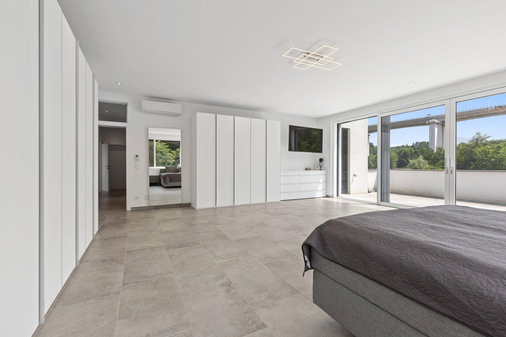 Geräumiges Schlafzimmer mit großen Schiebetüren zur Terrasse, Einbauschränken und Fliesenboden.