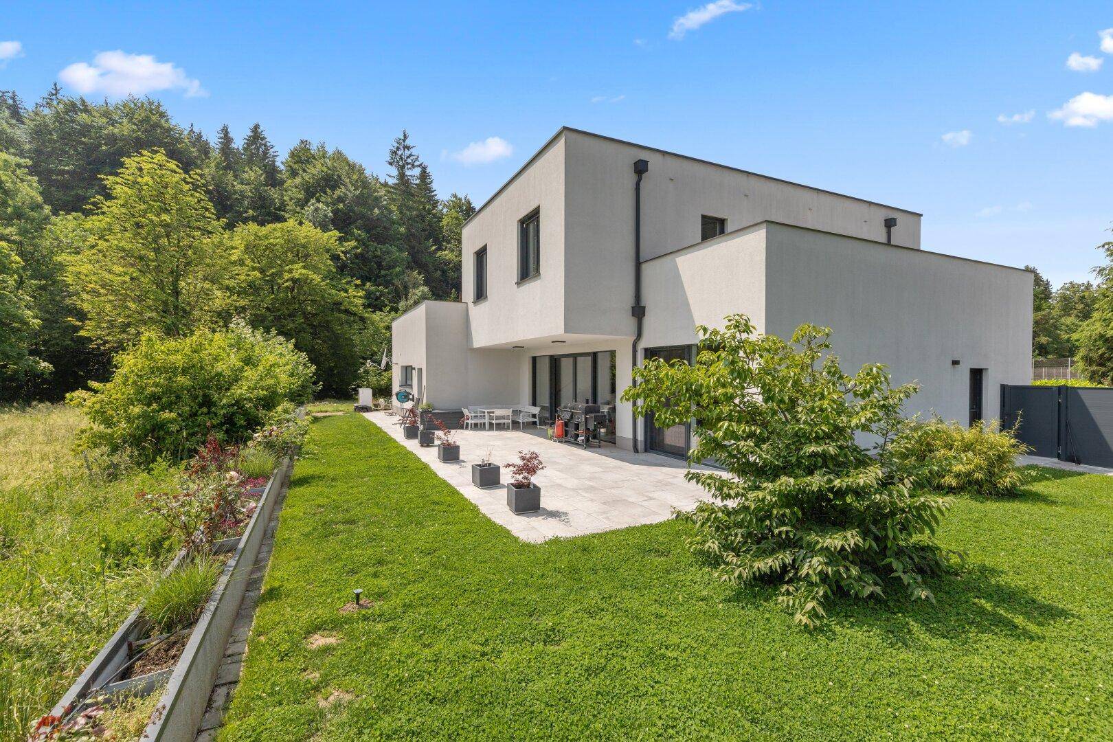 Seitliche Ansicht des Hauses mit großer, gepflasterter Terrasse und gepflegtem Rasenbereich.