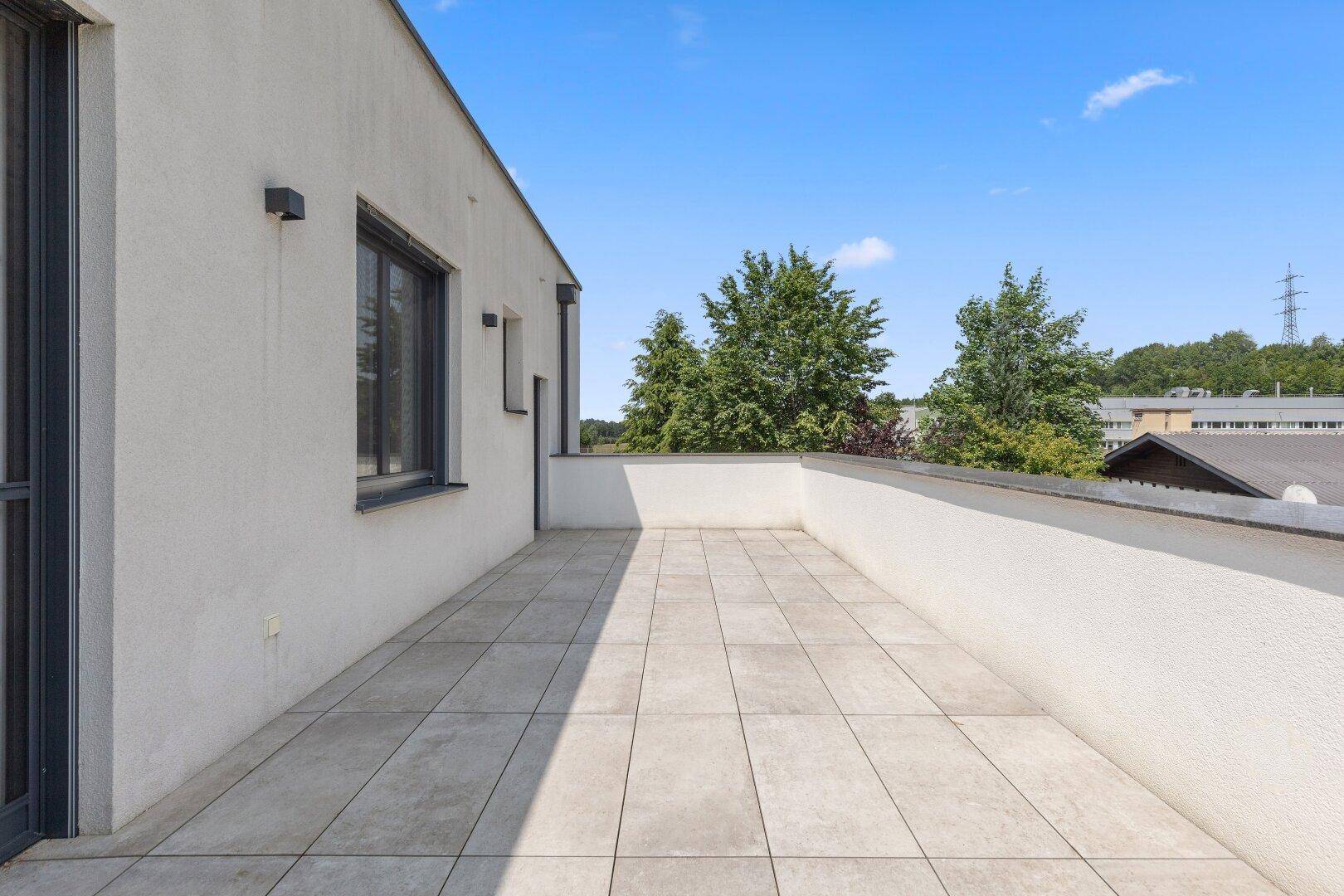 Geräumige Dachterrasse mit hellen Fliesen und weitem Blick in die Umgebung.
