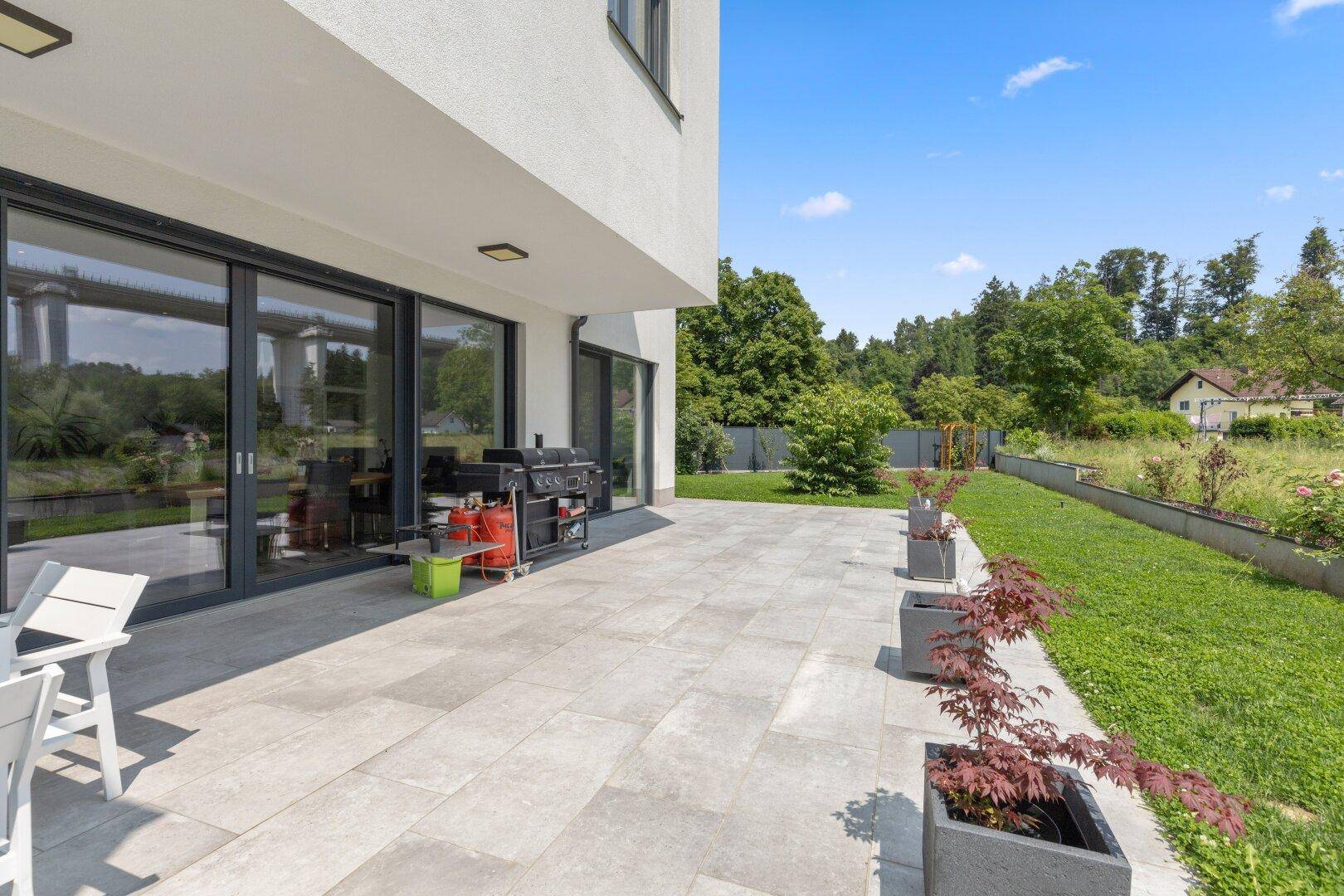 Geräumige Terrasse mit großformatigen Fliesen, Grillbereich und Zugang zum Innenraum durch Schiebetüren.