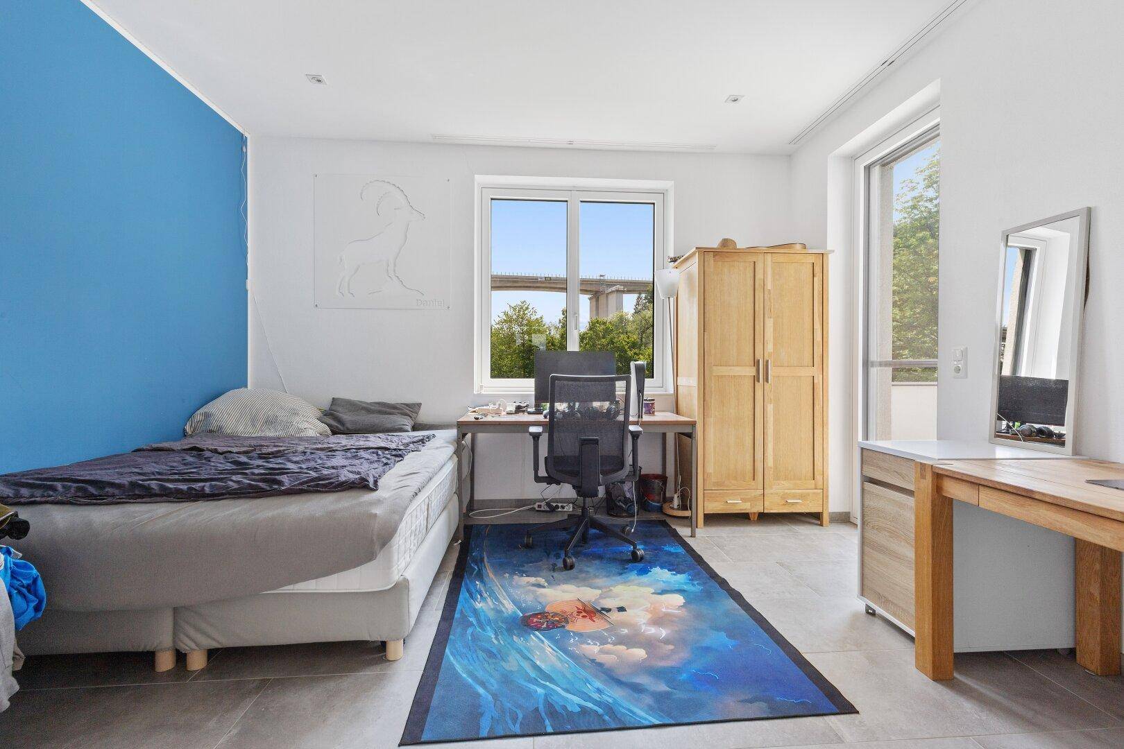 Jugendzimmer mit Bett, Schreibtisch und farbiger Wandakzentuierung.
