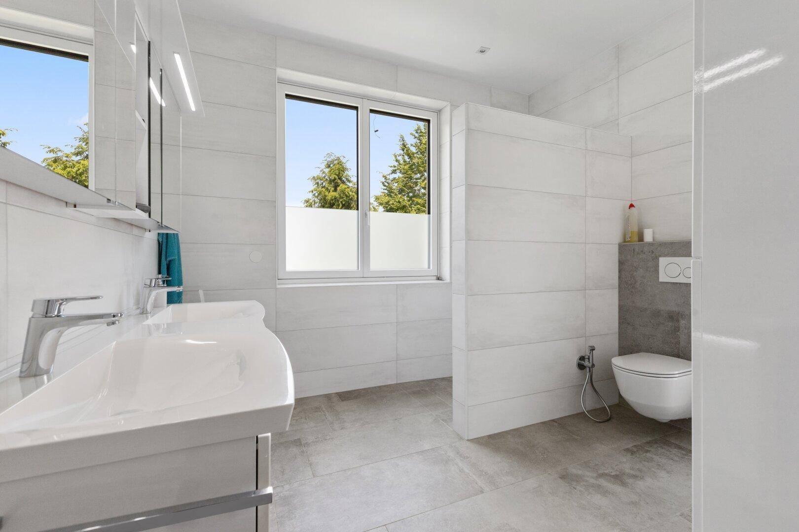 Modernes Badezimmer mit Doppelwaschbecken, wandhängendem WC und großem Fenster.