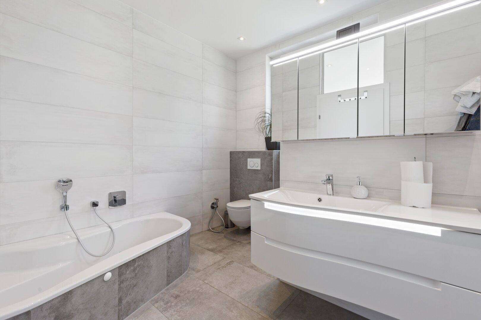 Zeitgemäßes Badezimmer mit Badewanne, wandhängendem WC und großem Spiegel über dem Waschtisch.