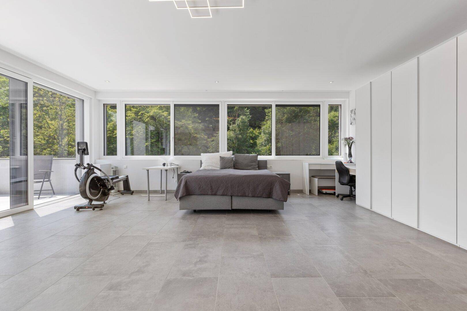 Helles Schlafzimmer mit breiter Fensterfront, Sportgeräten und viel Platz.
