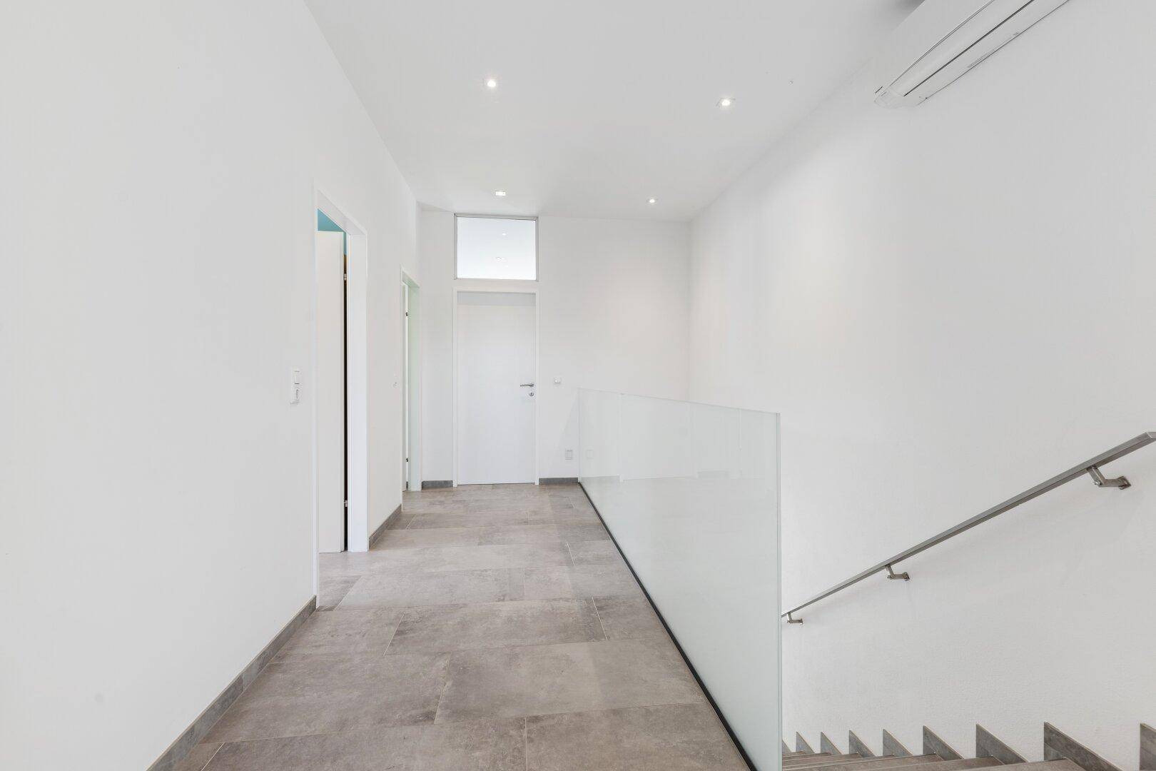 Heller Flur mit moderner Glasbrüstung an der Treppe und Fliesenboden.