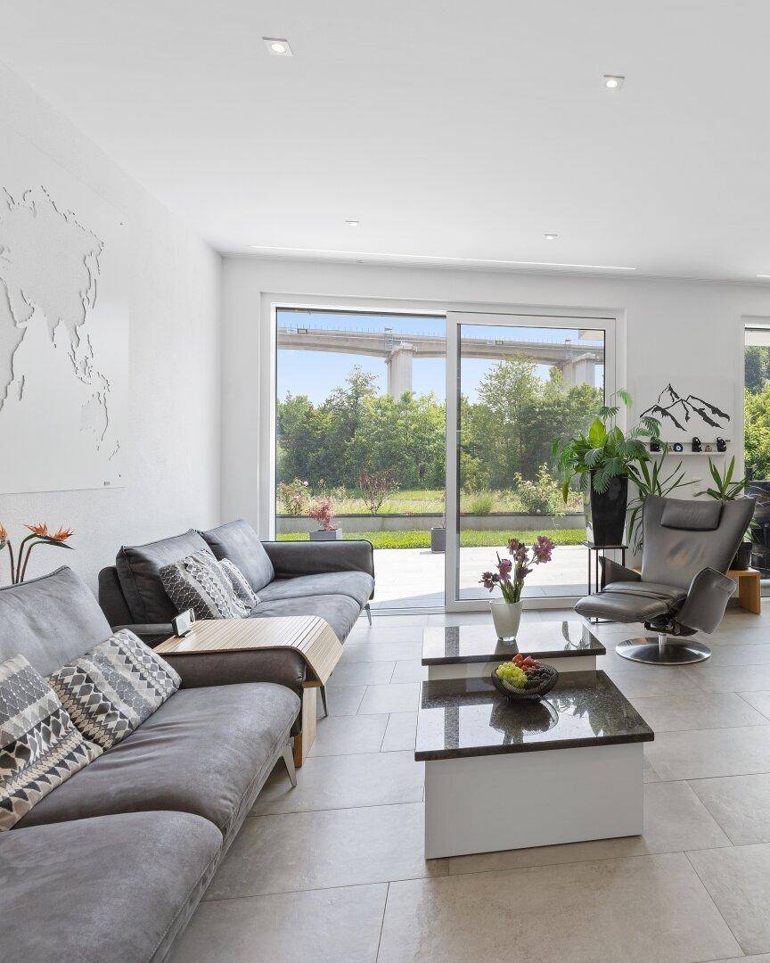 Gemütlicher Wohnbereich mit bequemen Sofas, Couchtischen und Blick ins Grüne durch große Fenster.