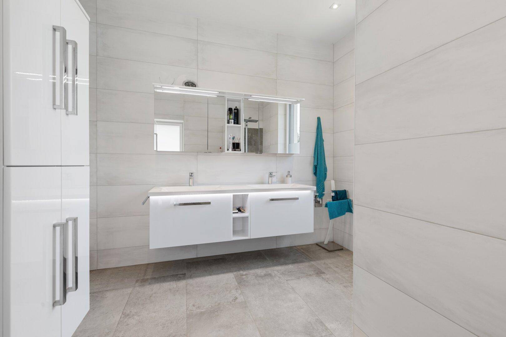 Elegantes Badezimmer mit schwebendem Doppelwaschtisch, Spiegelschrank und weißen Hochglanzschränken.