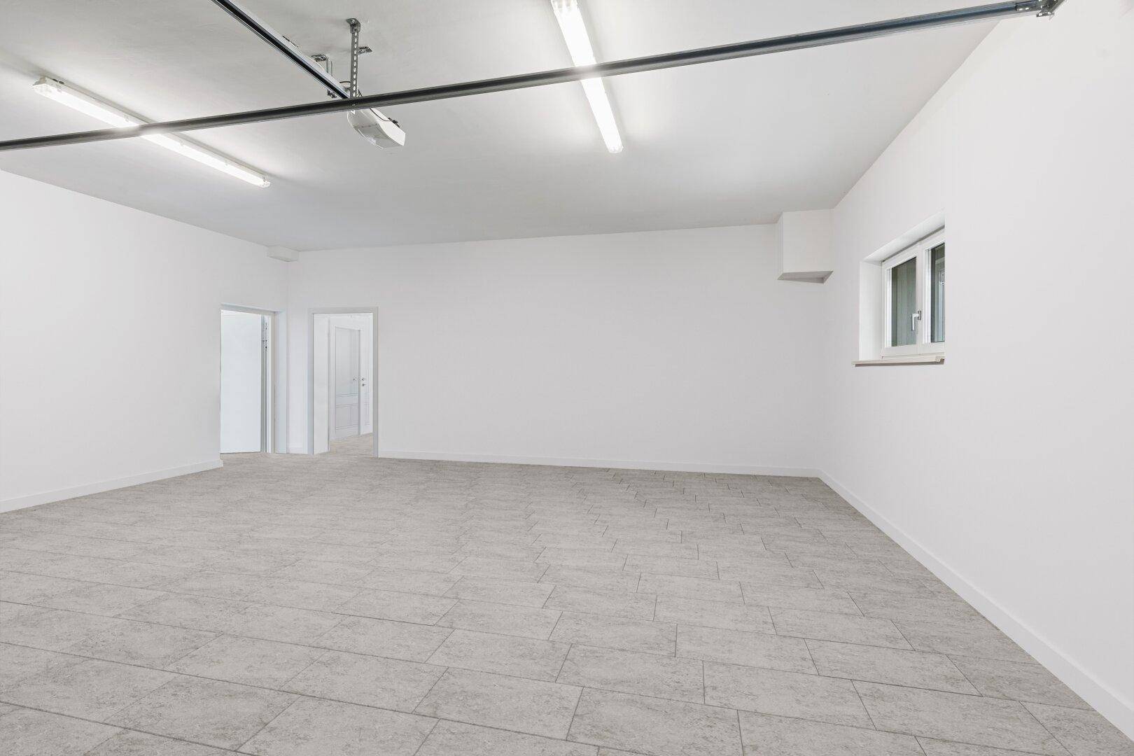 Geräumiger, leerer Raum mit Fliesenboden, weißen Wänden und Deckenbeleuchtung, ideal als Garage oder Lagerfläche.