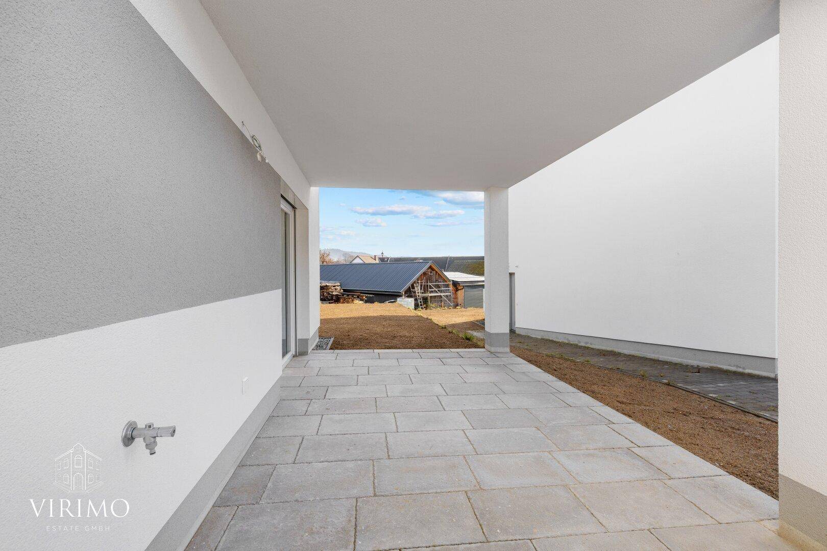Überdachte Terrasse mit Fliesenboden und Blick auf die grüne Umgebung.