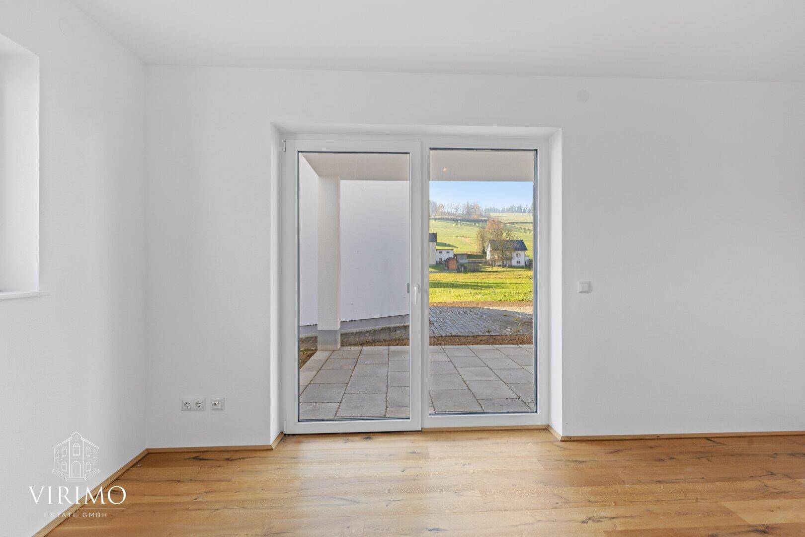 Heller Raum mit Holzboden und direktem Zugang zu einer gepflasterten Terrasse im Freien.