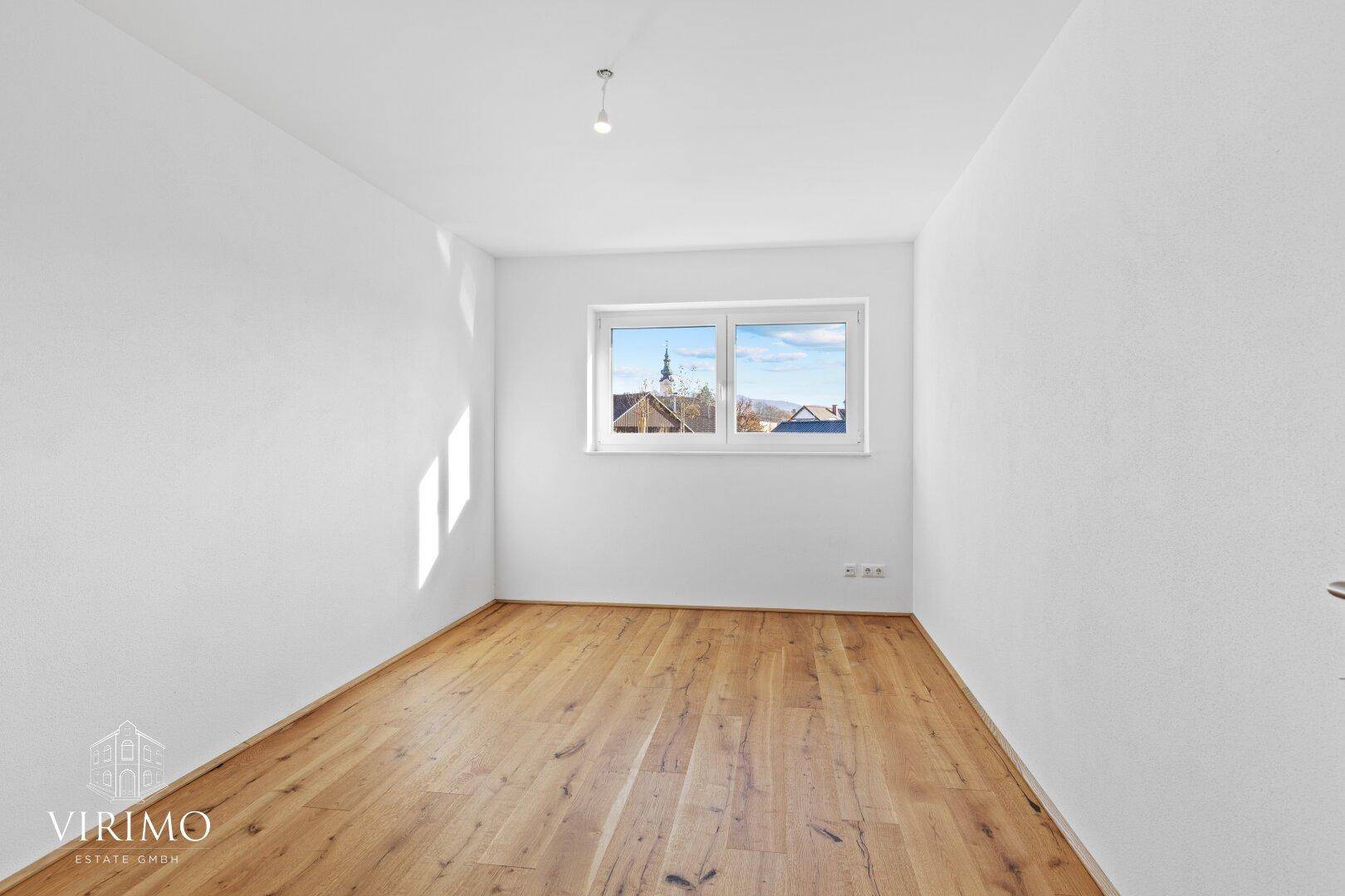 Leeres Schlafzimmer mit Holzboden und Fenster, das einen Blick auf die Umgebung bietet.