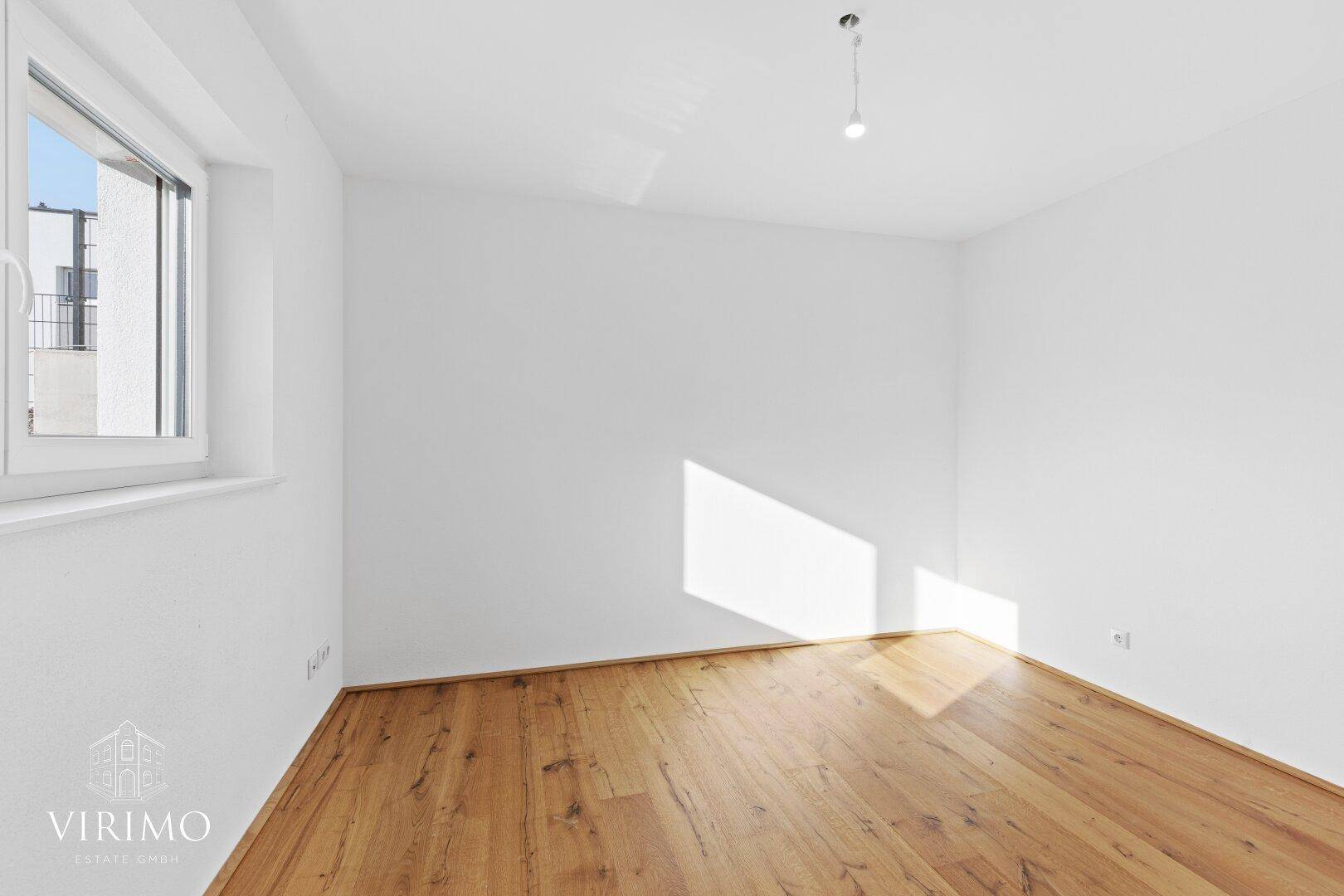 Helles Zimmer mit Holzboden und Fenster, das viel Sonnenlicht in den Raum lässt.