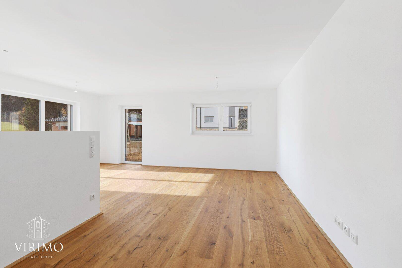 Heller, leerer Wohnbereich mit hochwertigem Holzboden und großen Fenstern für viel Tageslicht.