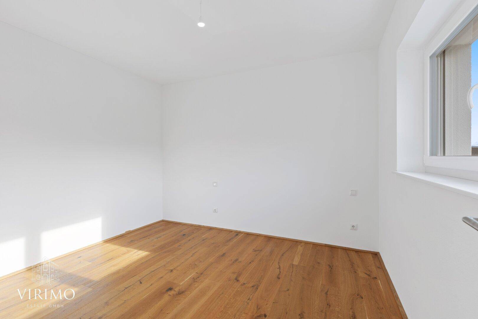 Helles Schlafzimmer mit Holzboden und großem Fenster, bereit für individuelle Gestaltung.