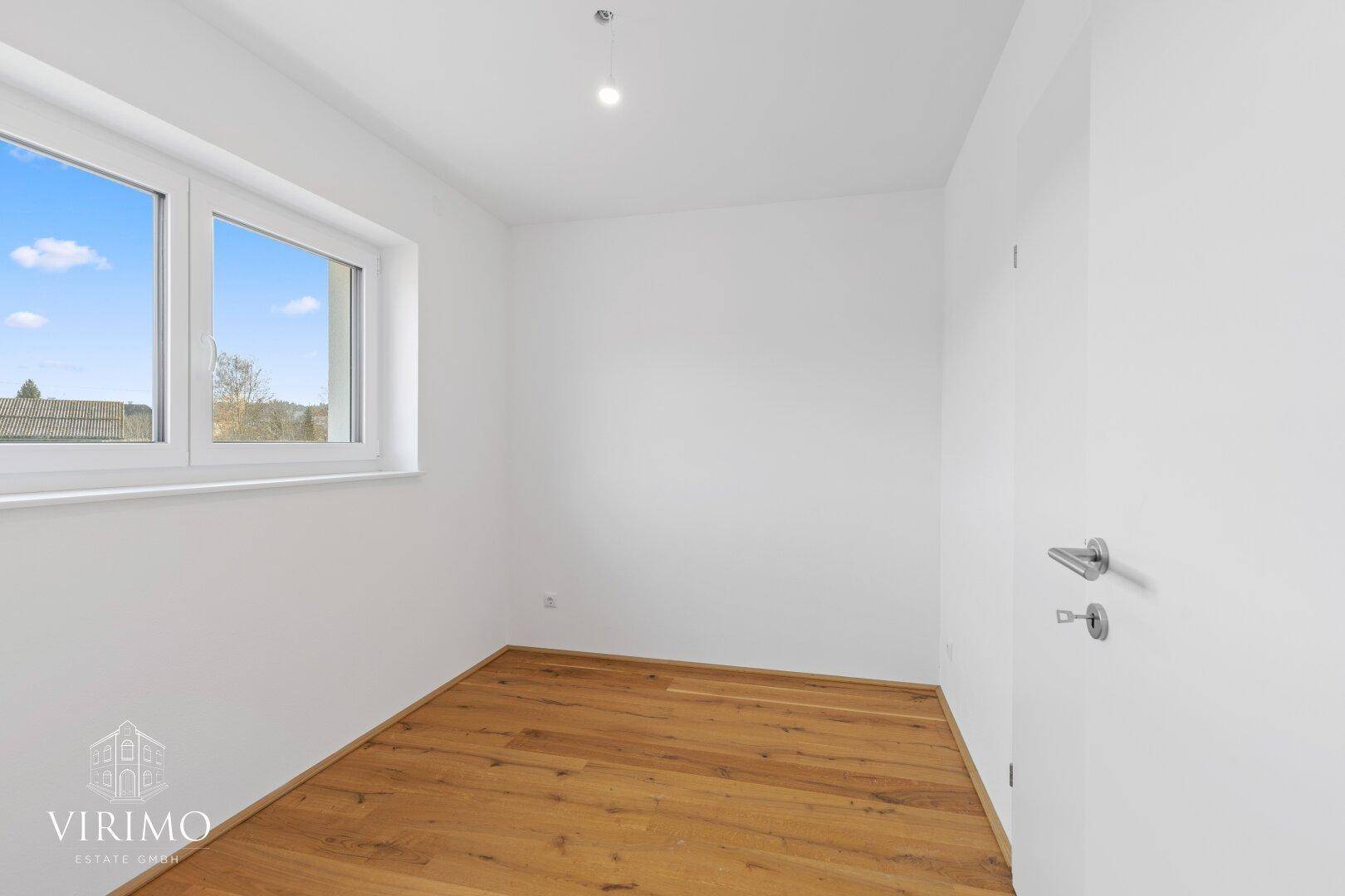 Helles Schlafzimmer mit Holzboden und Fenster, bietet einen weiten Blick in die Landschaft.
