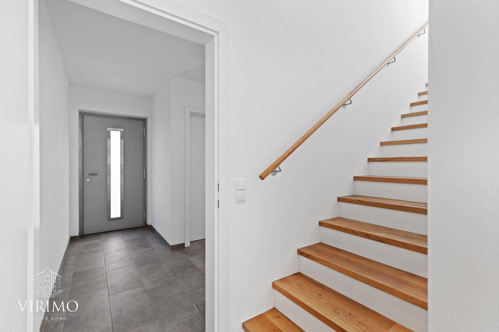 Moderner Eingangsbereich mit grauen Fliesen, einer stilvollen Haustür und einer Holztreppe.