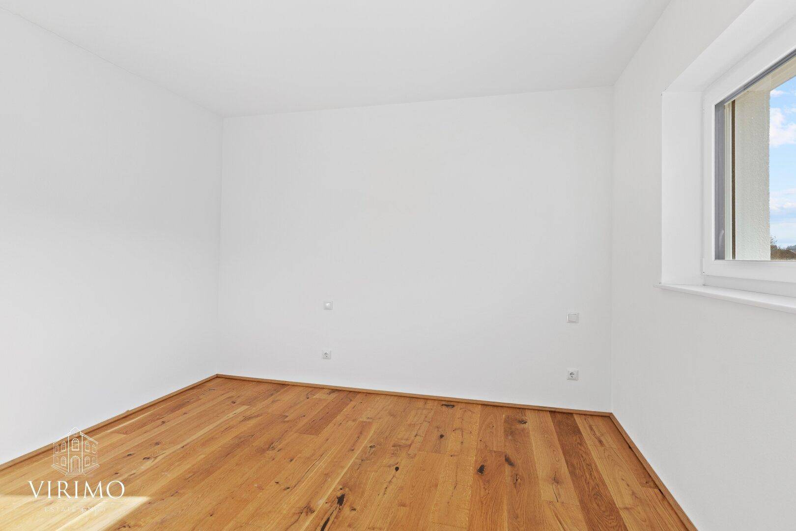 Ruhiges Schlafzimmer mit Holzboden, weißen Wänden und einem Fenster für natürliches Licht.