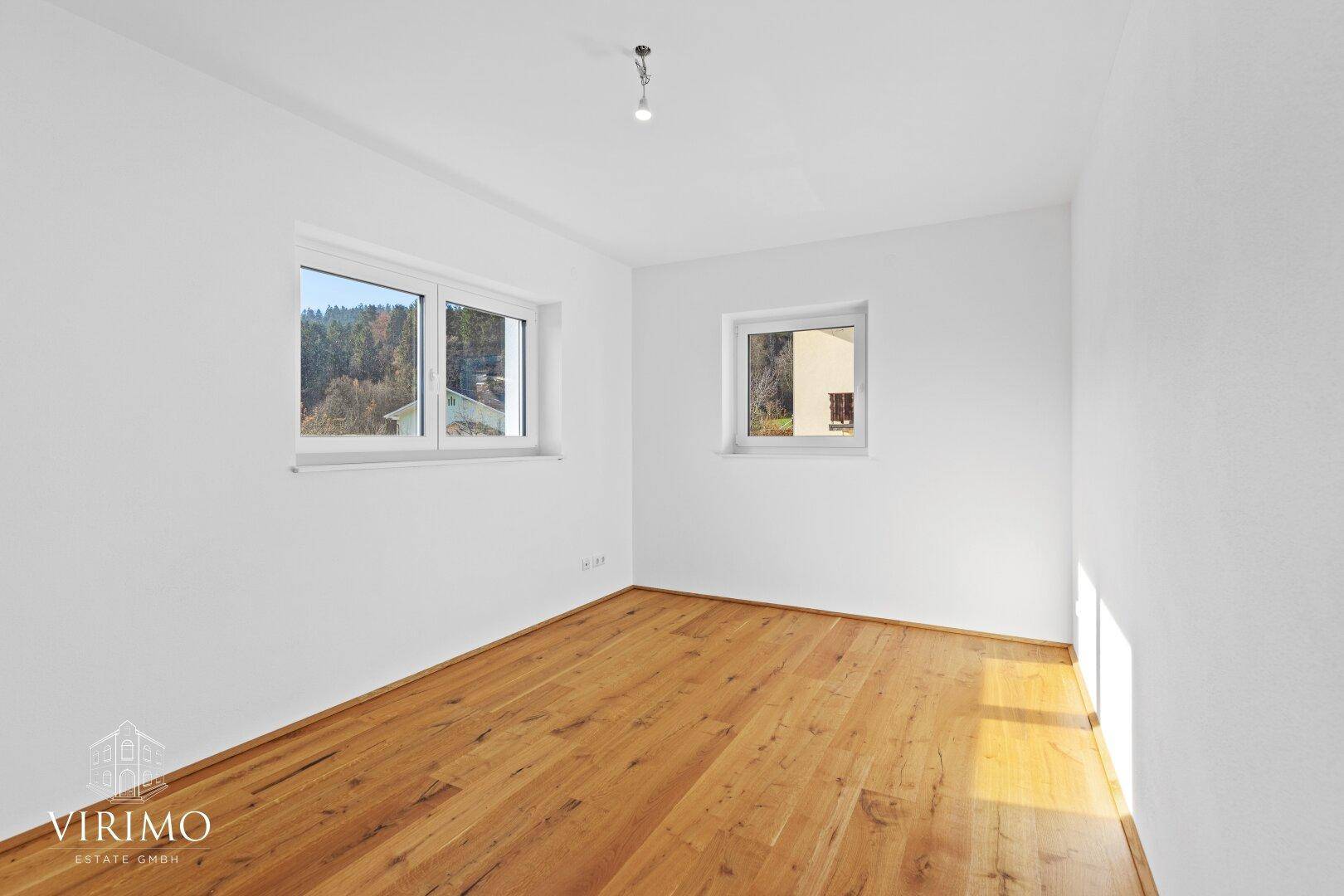 Helles Schlafzimmer mit Holzboden, weißen Wänden und zwei Fenstern für viel Tageslicht.