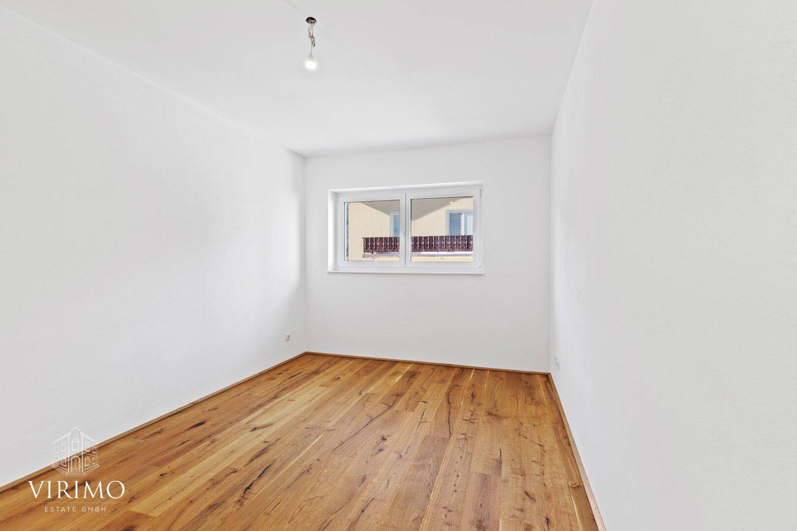 Gemütliches Schlafzimmer mit Holzboden, weißen Wänden und einem Fenster mit Blick nach draußen.